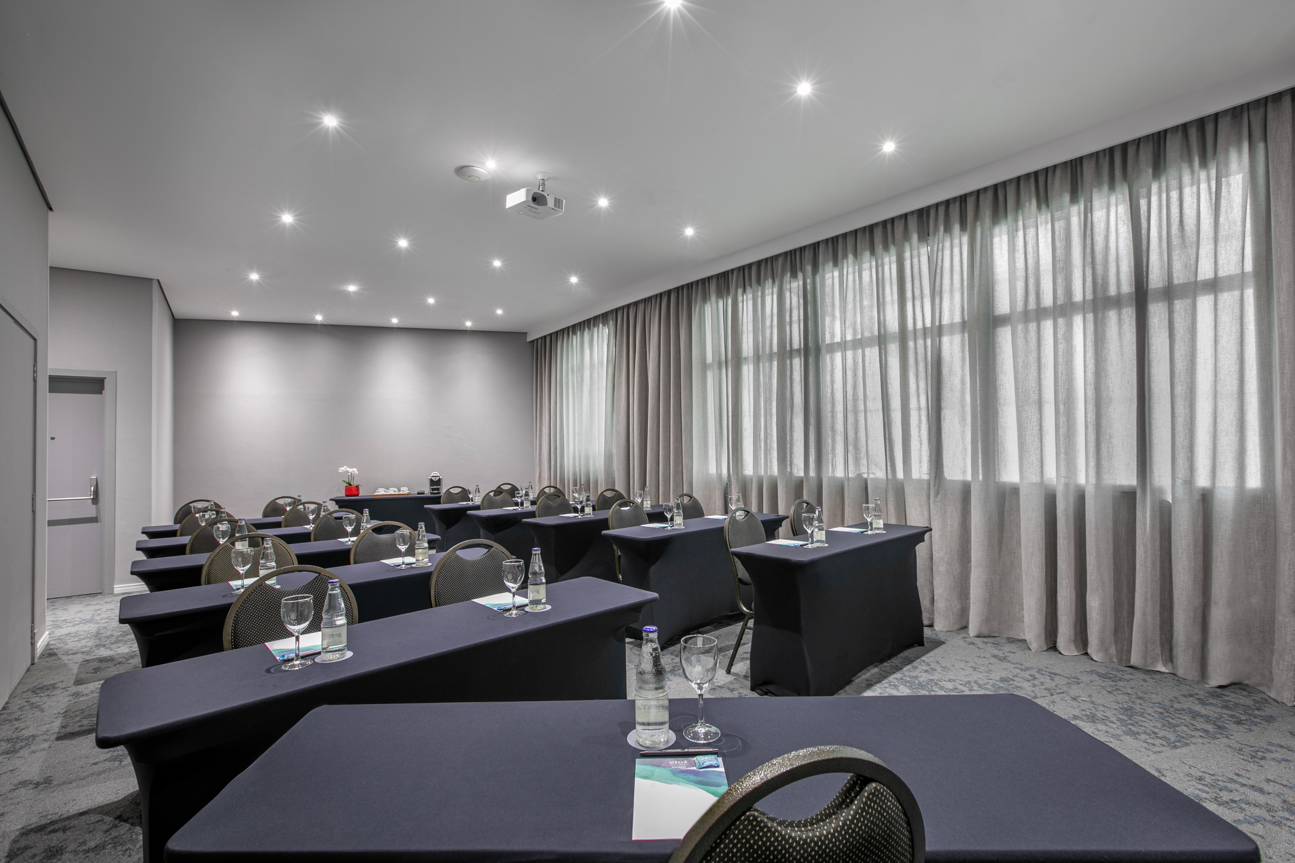 Modern conference room with dark tables, projector, grey curtains, and organized seating.
