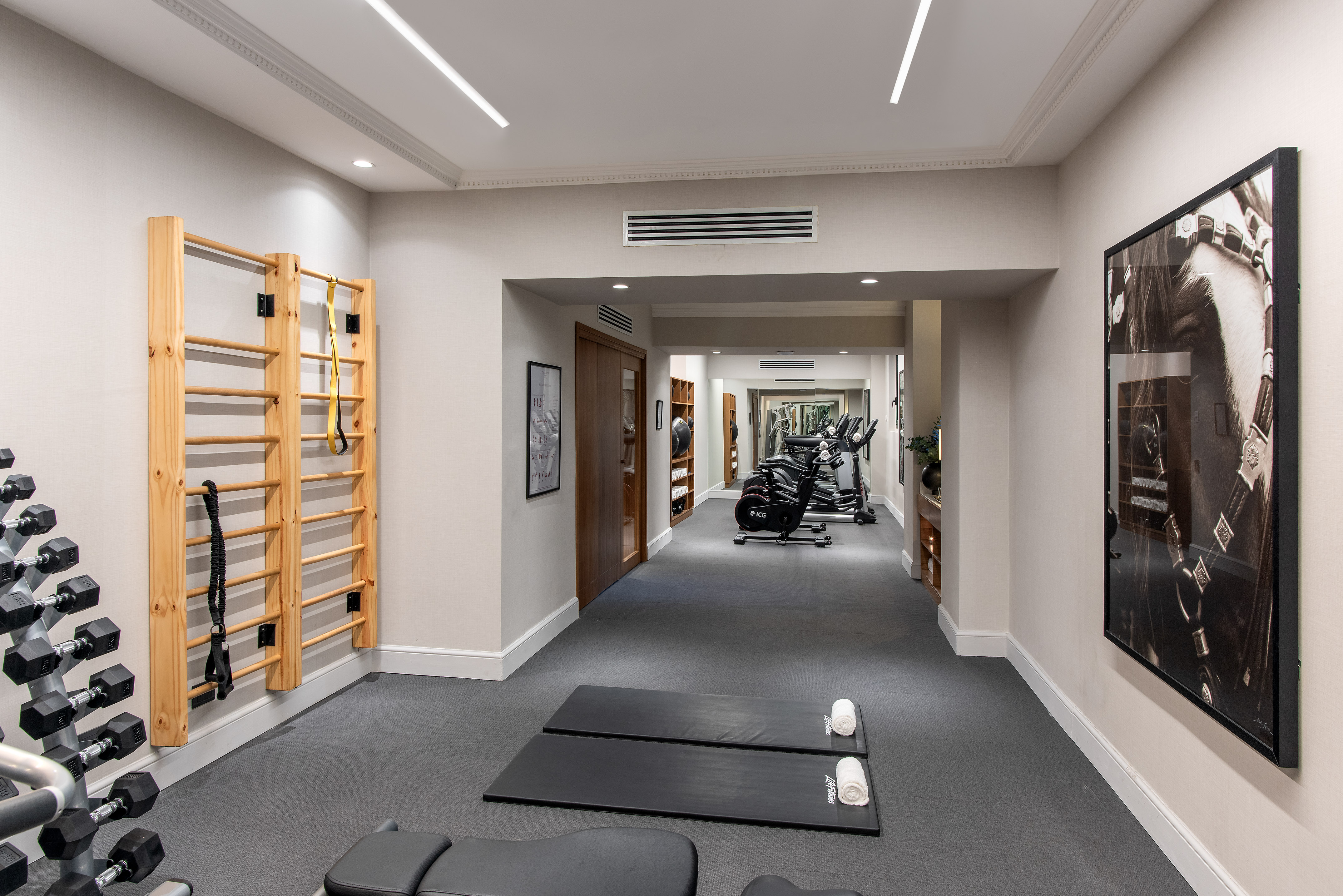 Hotel gym with wall bars, dumbbells, exercise mats, and cardio machines.