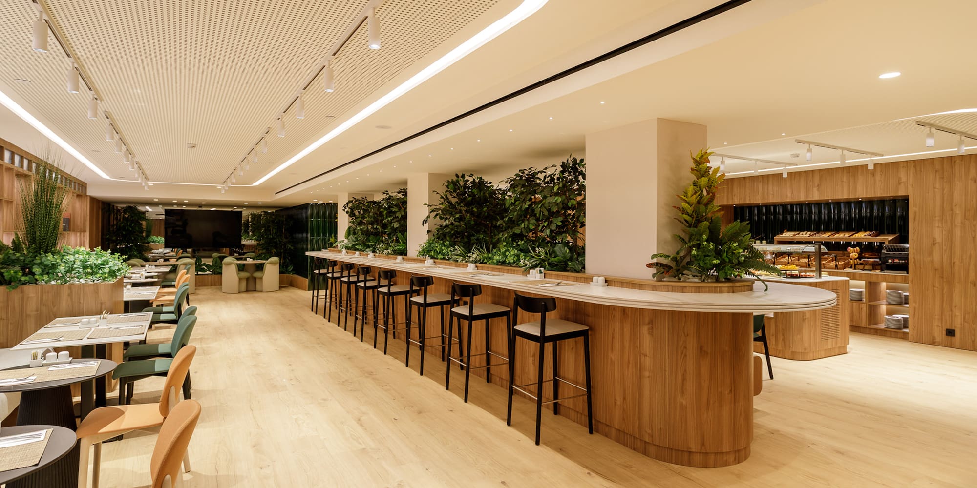Modern restaurant buffet with long bar, wood, and green plants.