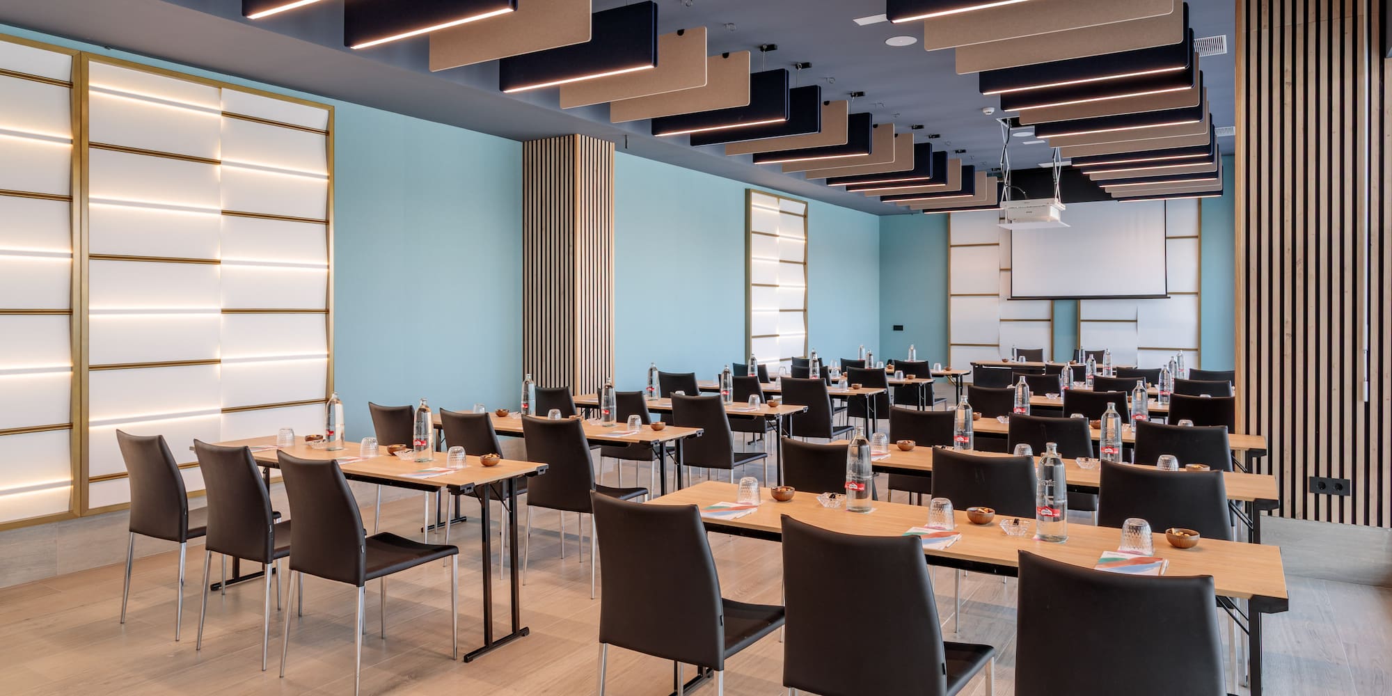 Modern conference room with light blue walls, wooden tables, and projector.