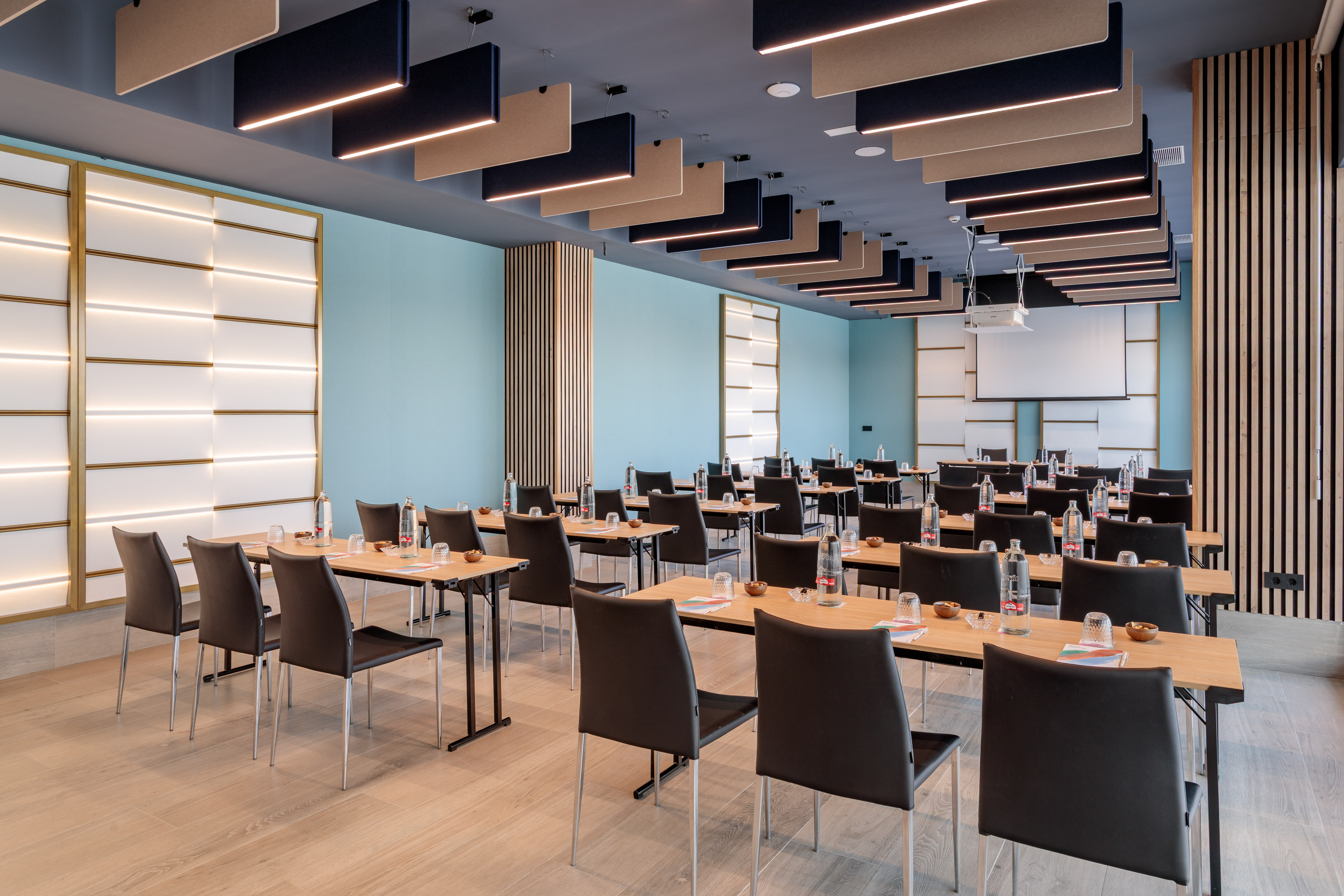 Modern conference room with light blue walls, wooden tables, and projector.