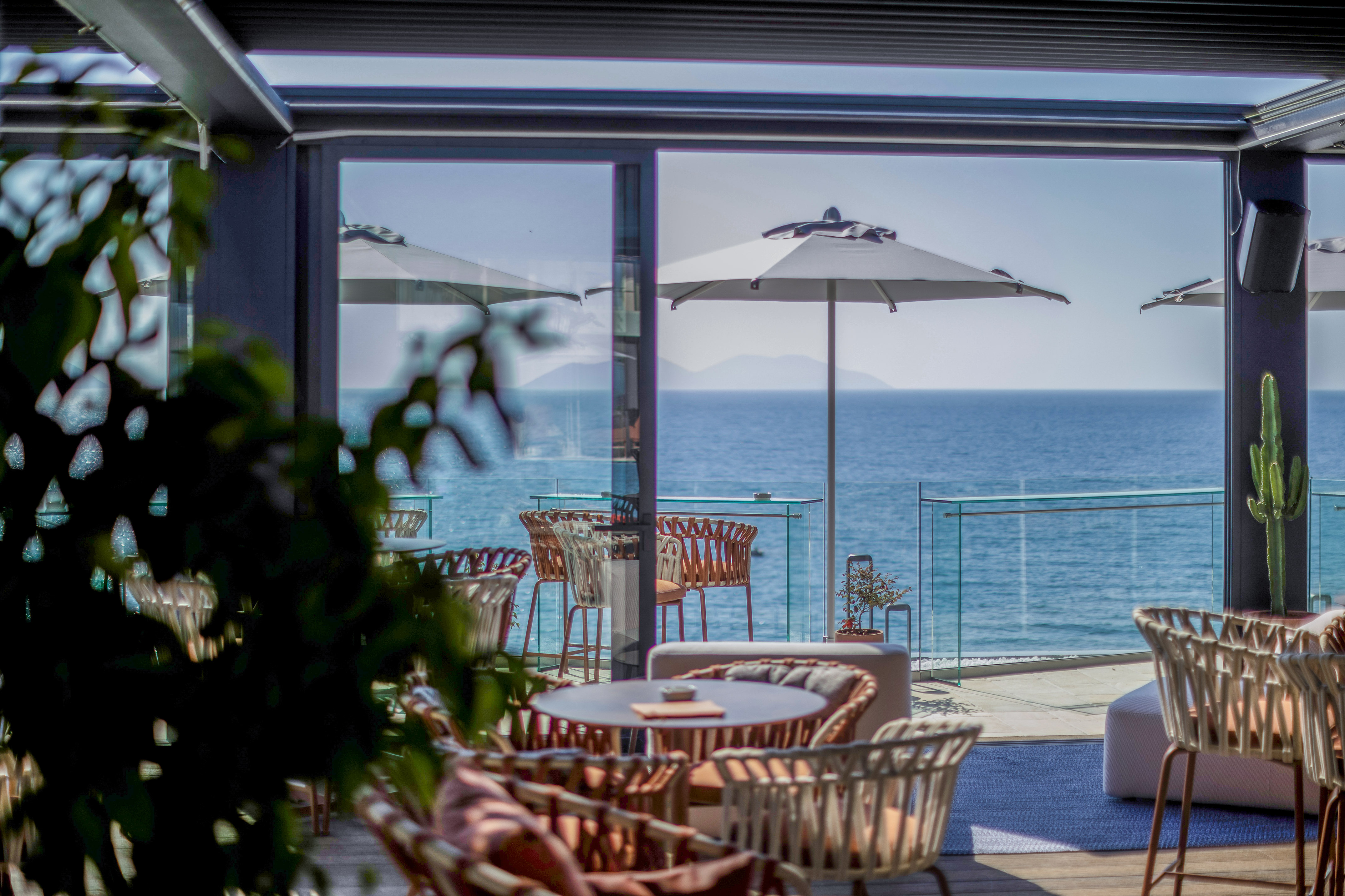 Sunny seaside cafe terrace with outdoor tables, chairs, umbrellas, and ocean view.