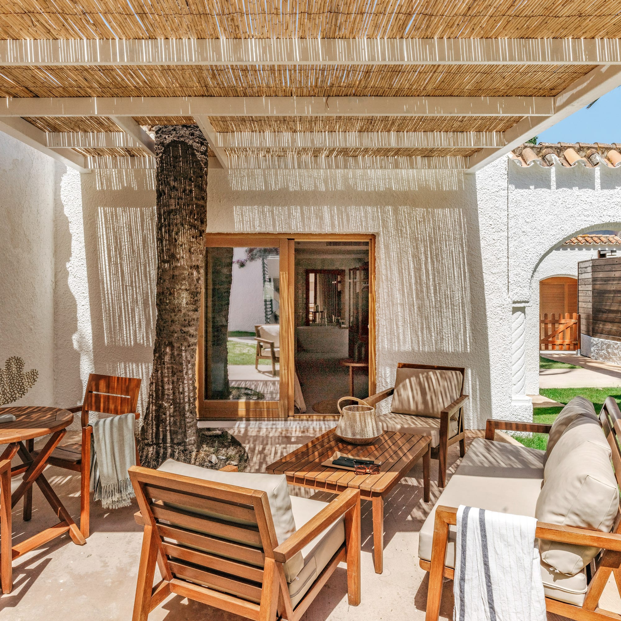 Sunny resort patio with wooden furniture, rattan canopy, and palm tree.