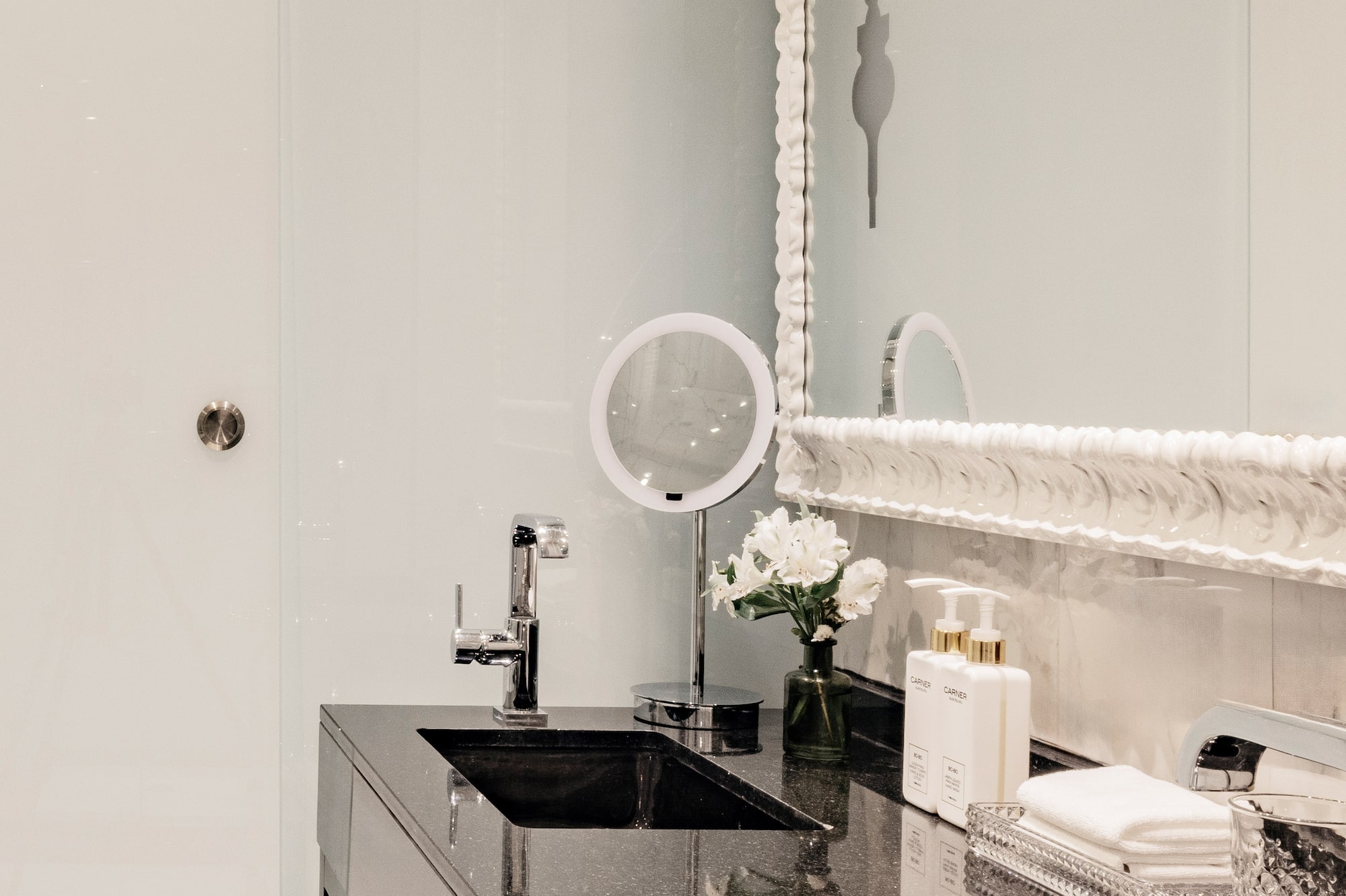 Baño moderno con lavabos dobles negros, espejo y detalles de lujo.