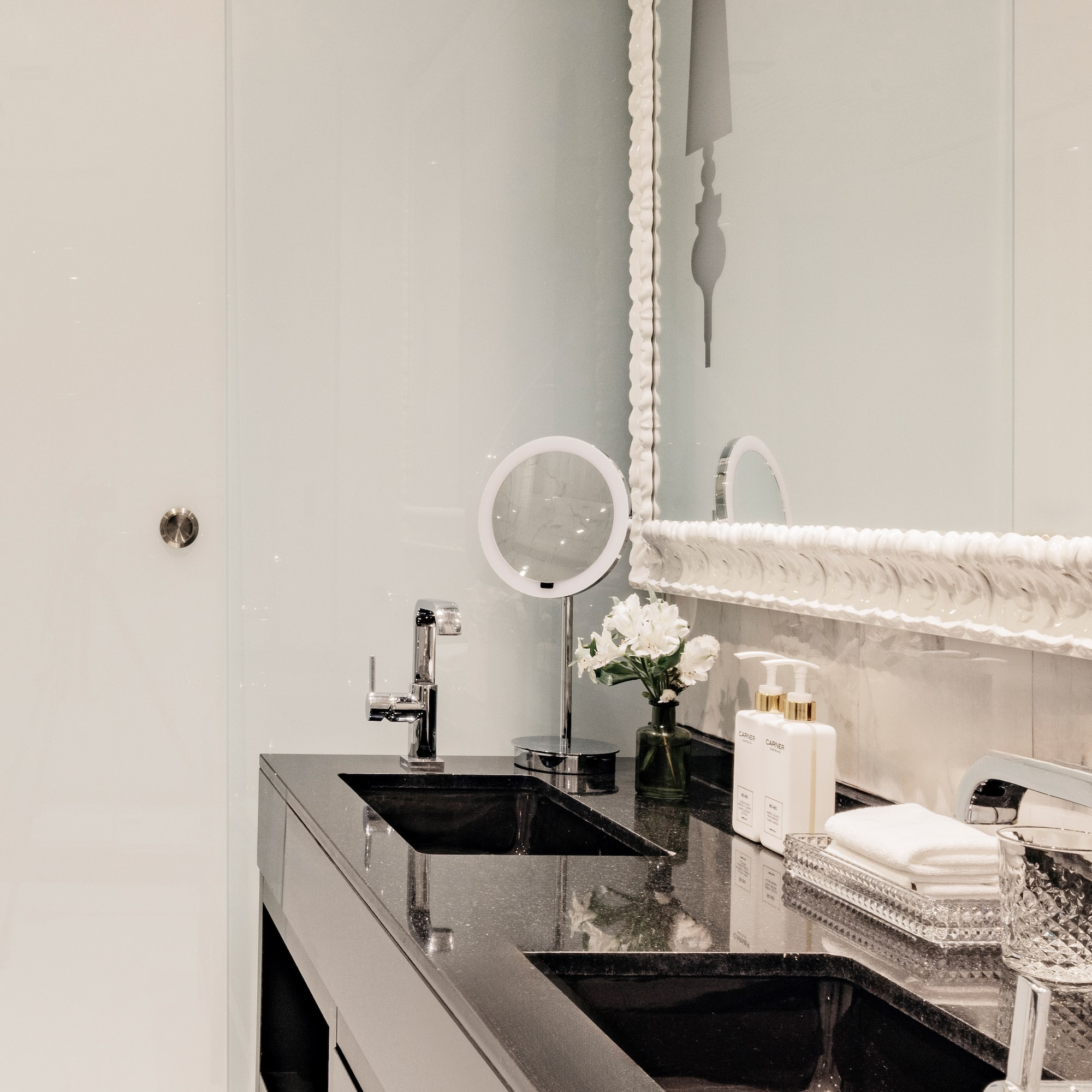 Baño moderno con lavabos dobles negros, espejo y detalles de lujo.