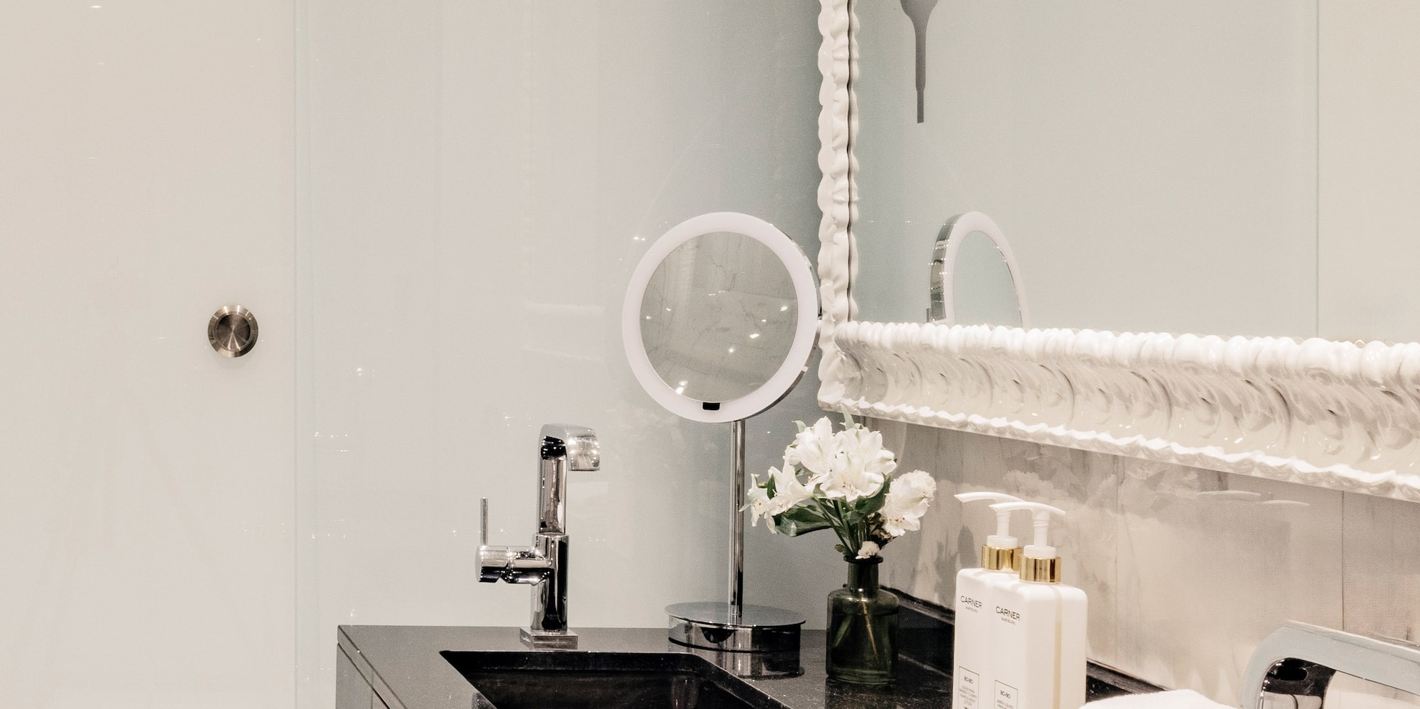 Baño moderno con lavabos dobles negros, espejo y detalles de lujo.