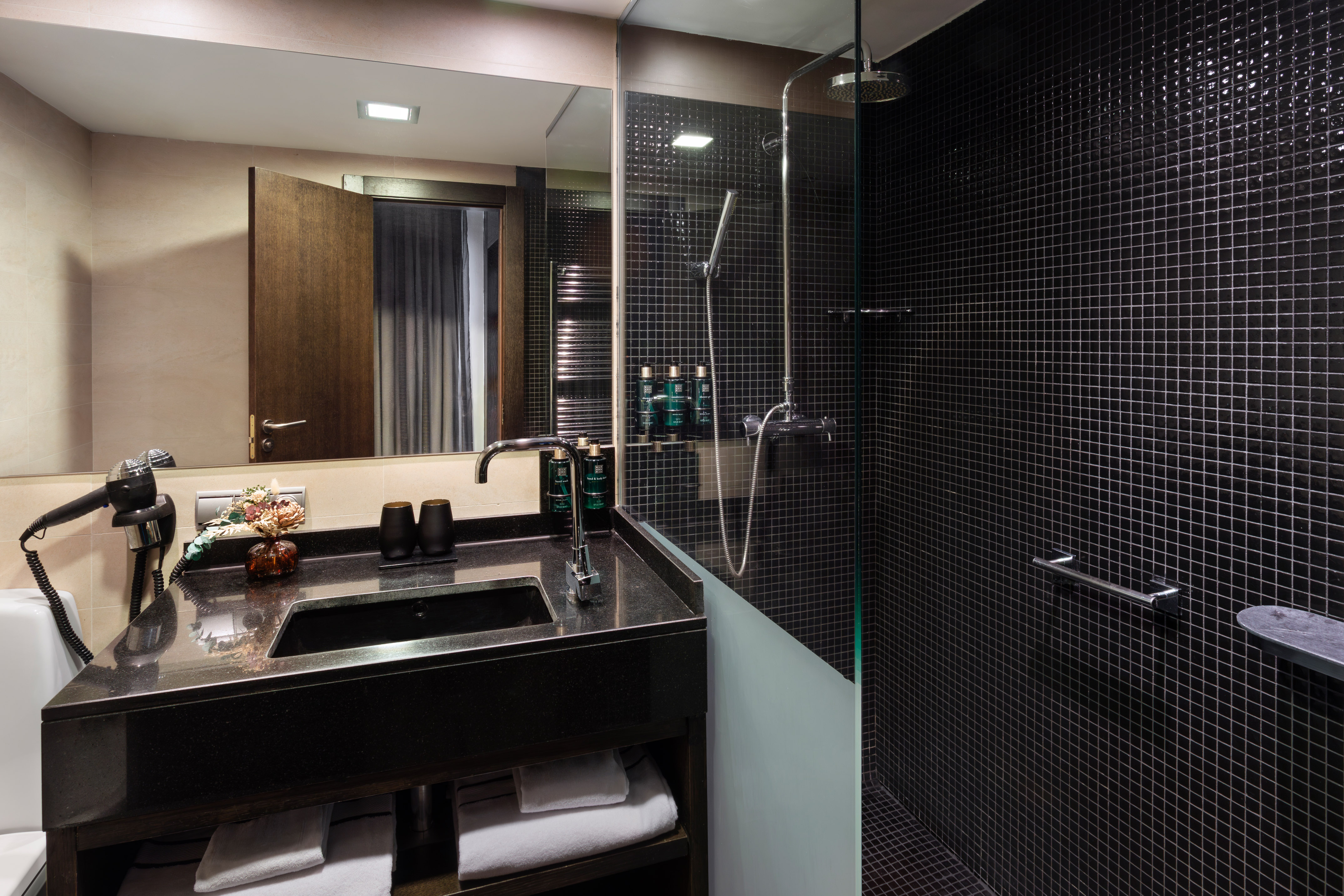 Modern bathroom with black tiled shower, vanity, sink, and large mirror.