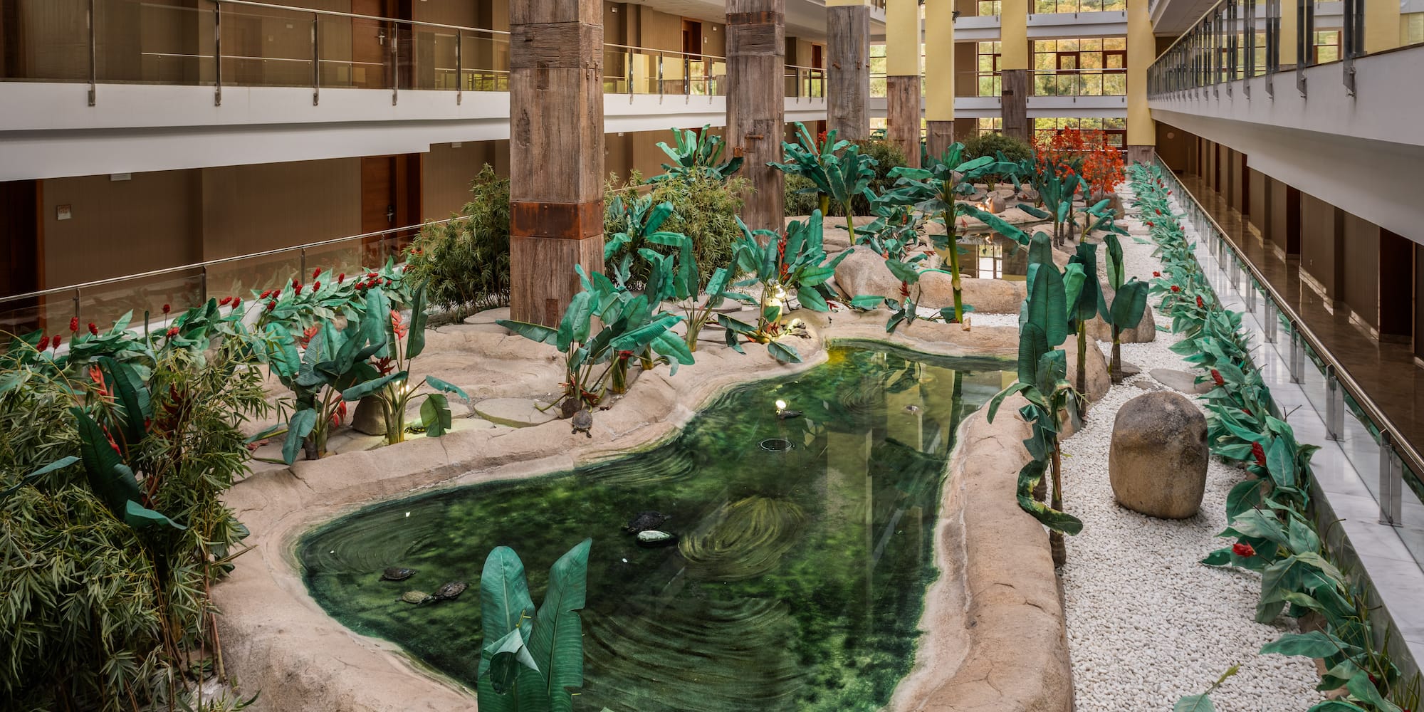Hotel atrium garden with tropical pond, turtles, lush plants, and multistory balconies.