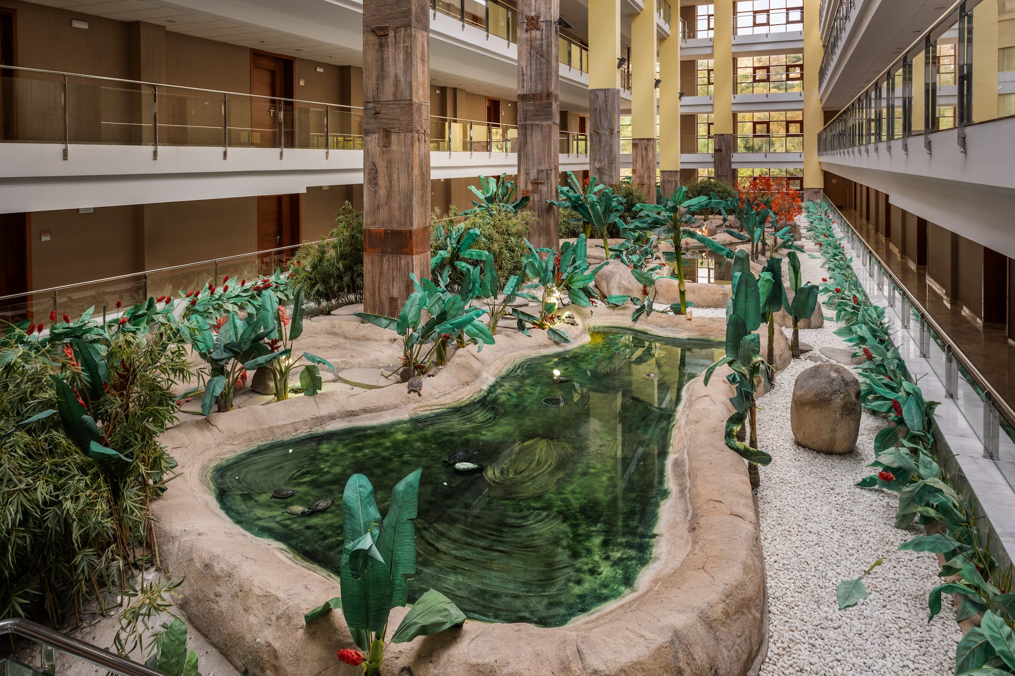 Hotel atrium garden with tropical pond, turtles, lush plants, and multistory balconies.