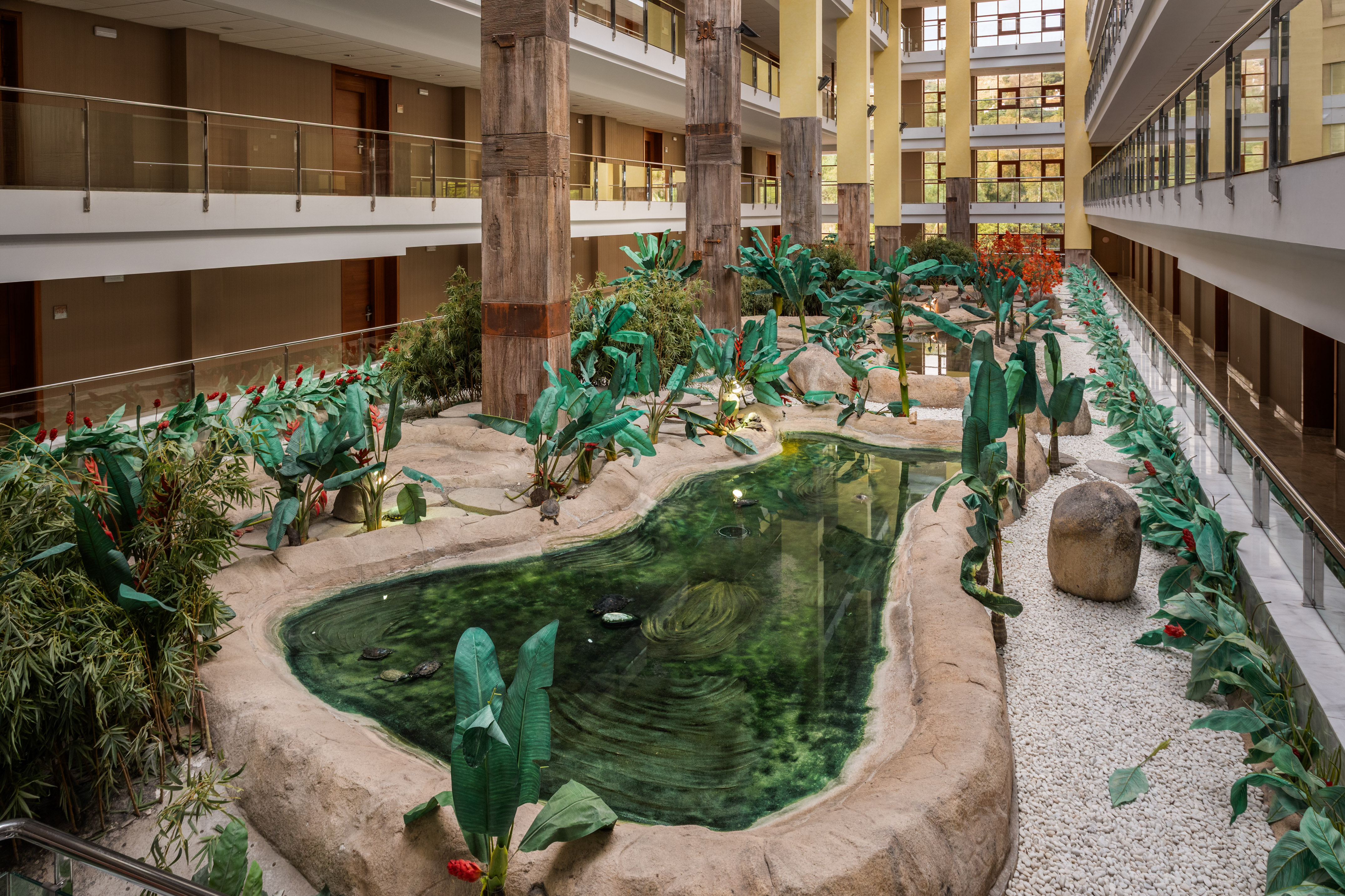 Hotel atrium garden with tropical pond, turtles, lush plants, and multistory balconies.