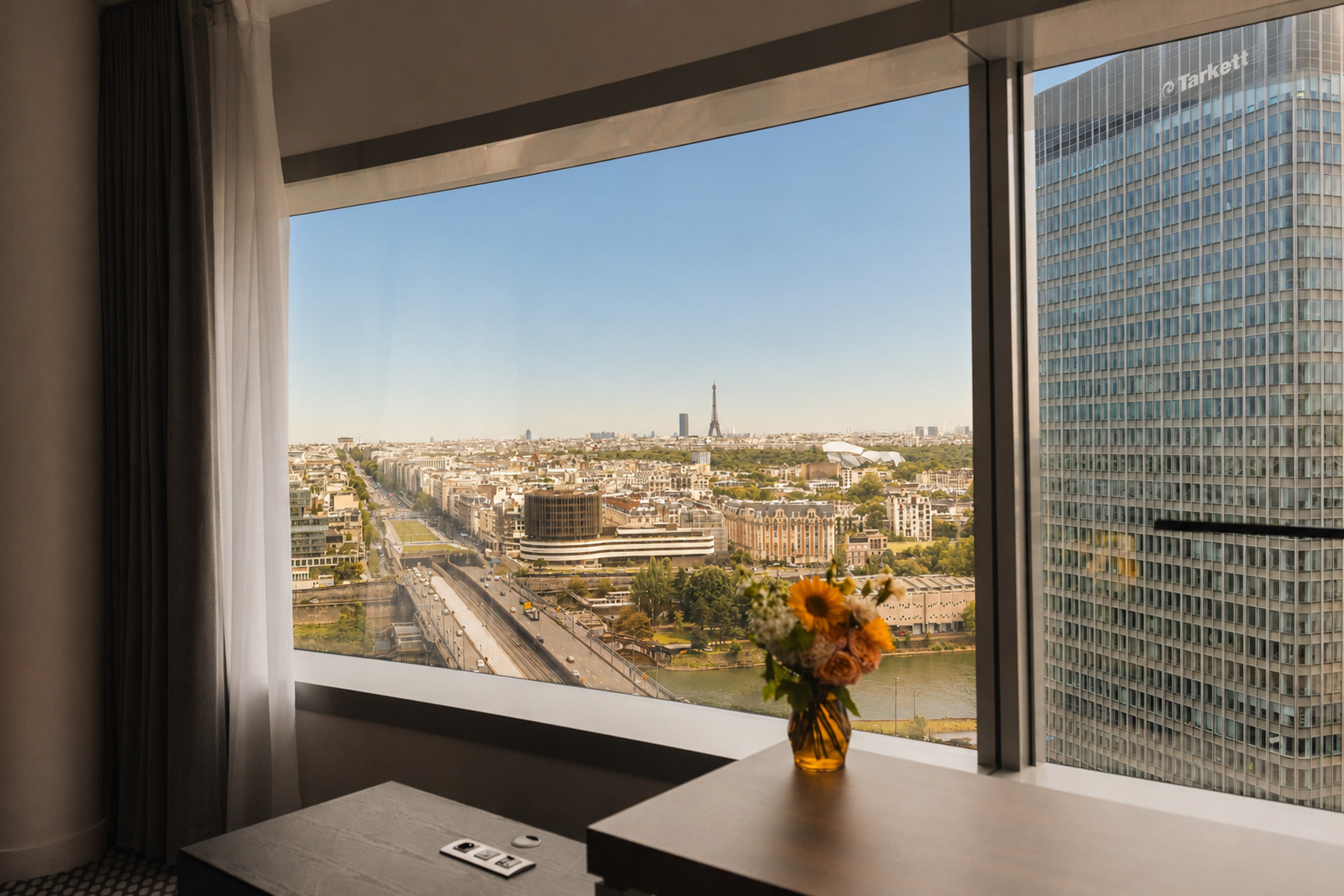 Paris skyline view from window: Eiffel Tower, Seine River, modern buildings.