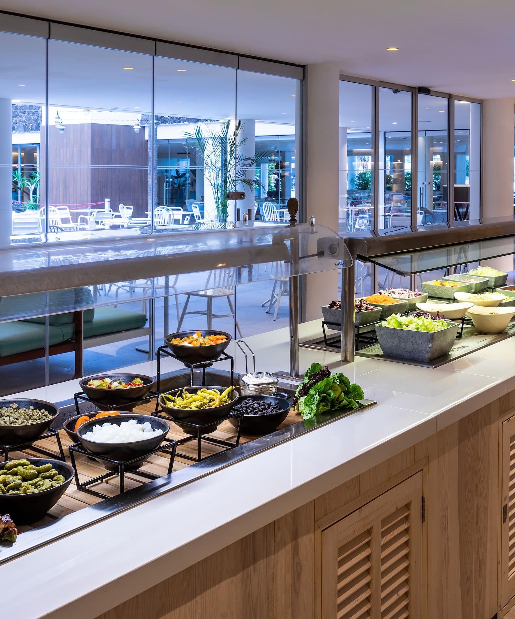 Hotel buffet salad bar with fresh vegetables, olives, and toppings.