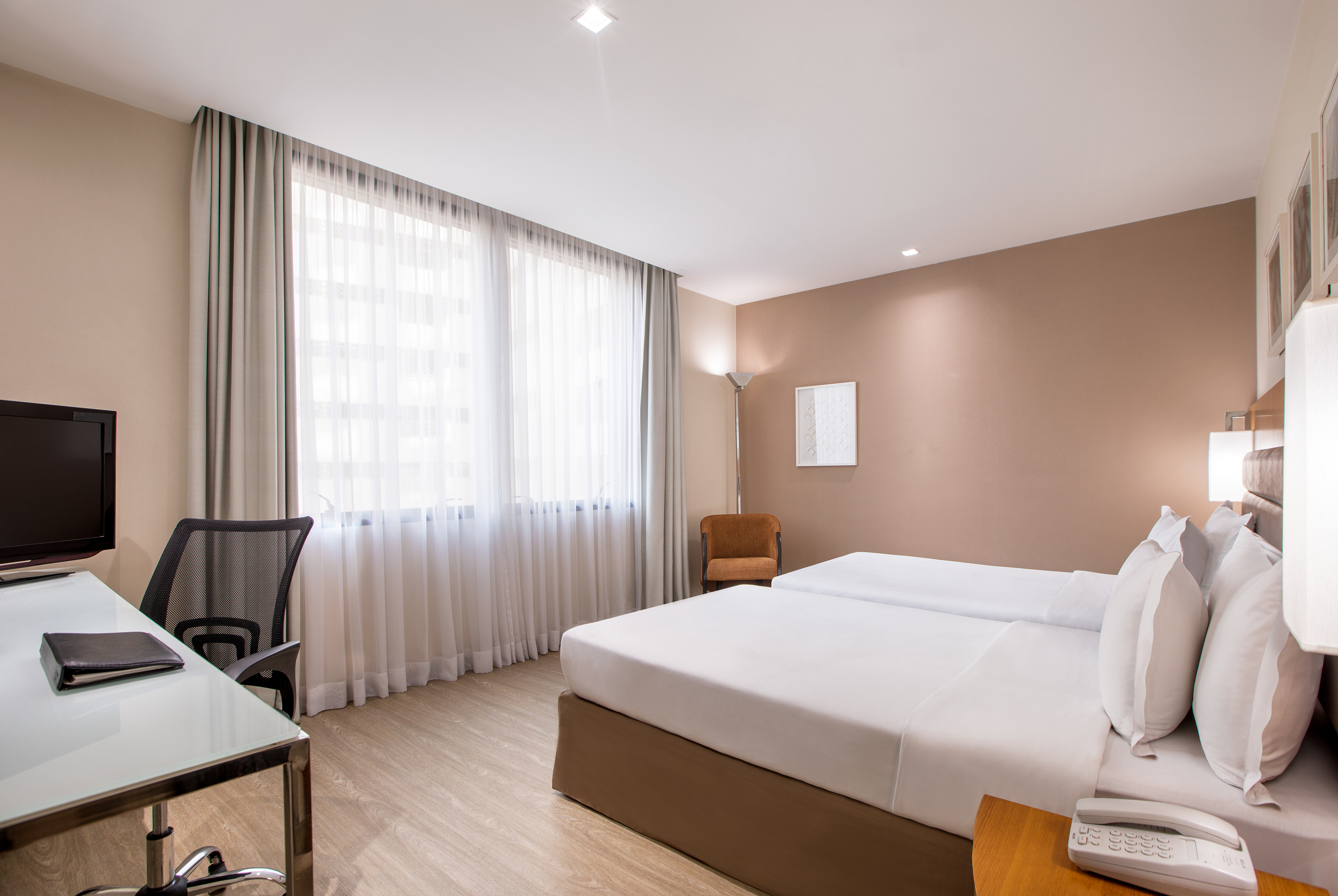 Clean, modern hotel room with twin beds, desk, and large window.