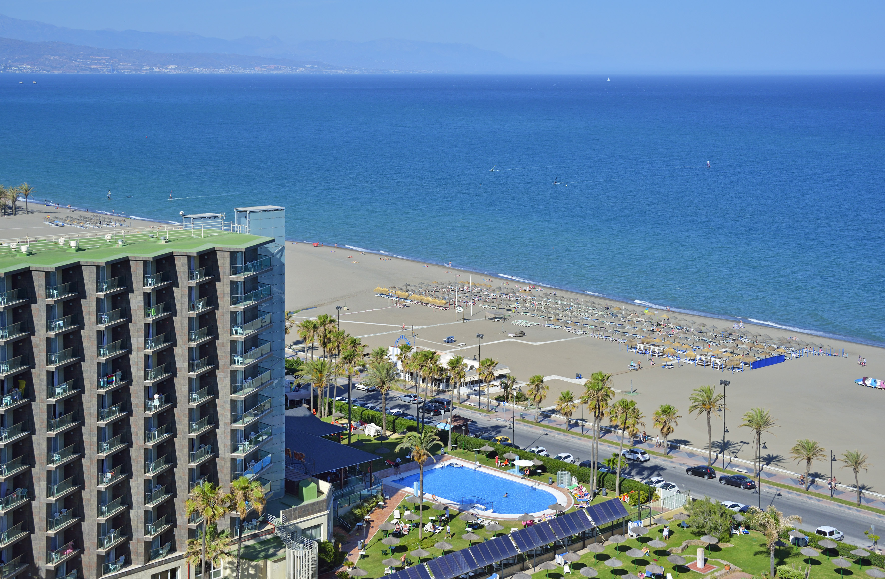 Beachfront resort hotel, pool, sandy beach with umbrellas, and blue sea.
