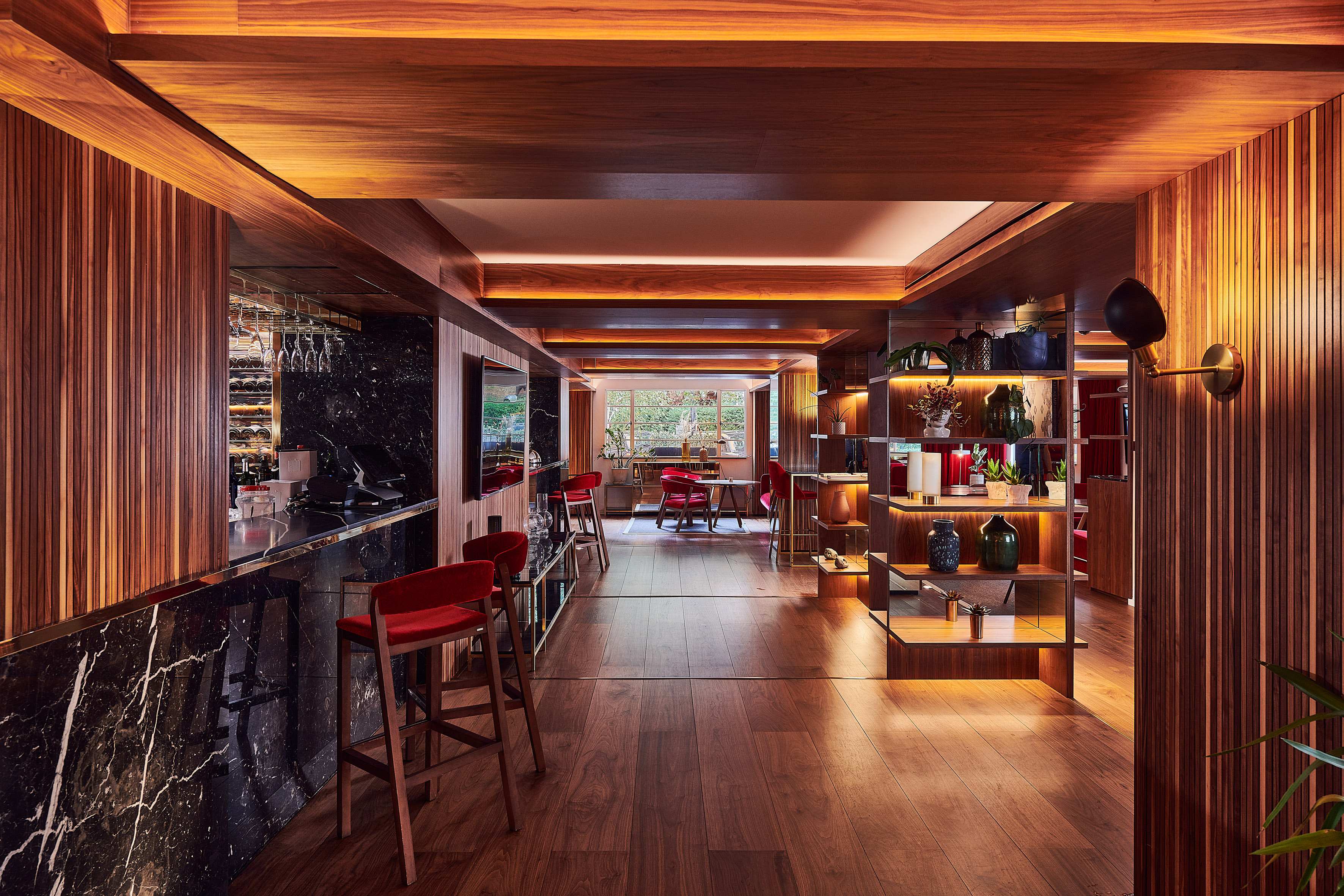 Warm wood bar lounge with black marble counter, red stools, and ambient lighting.