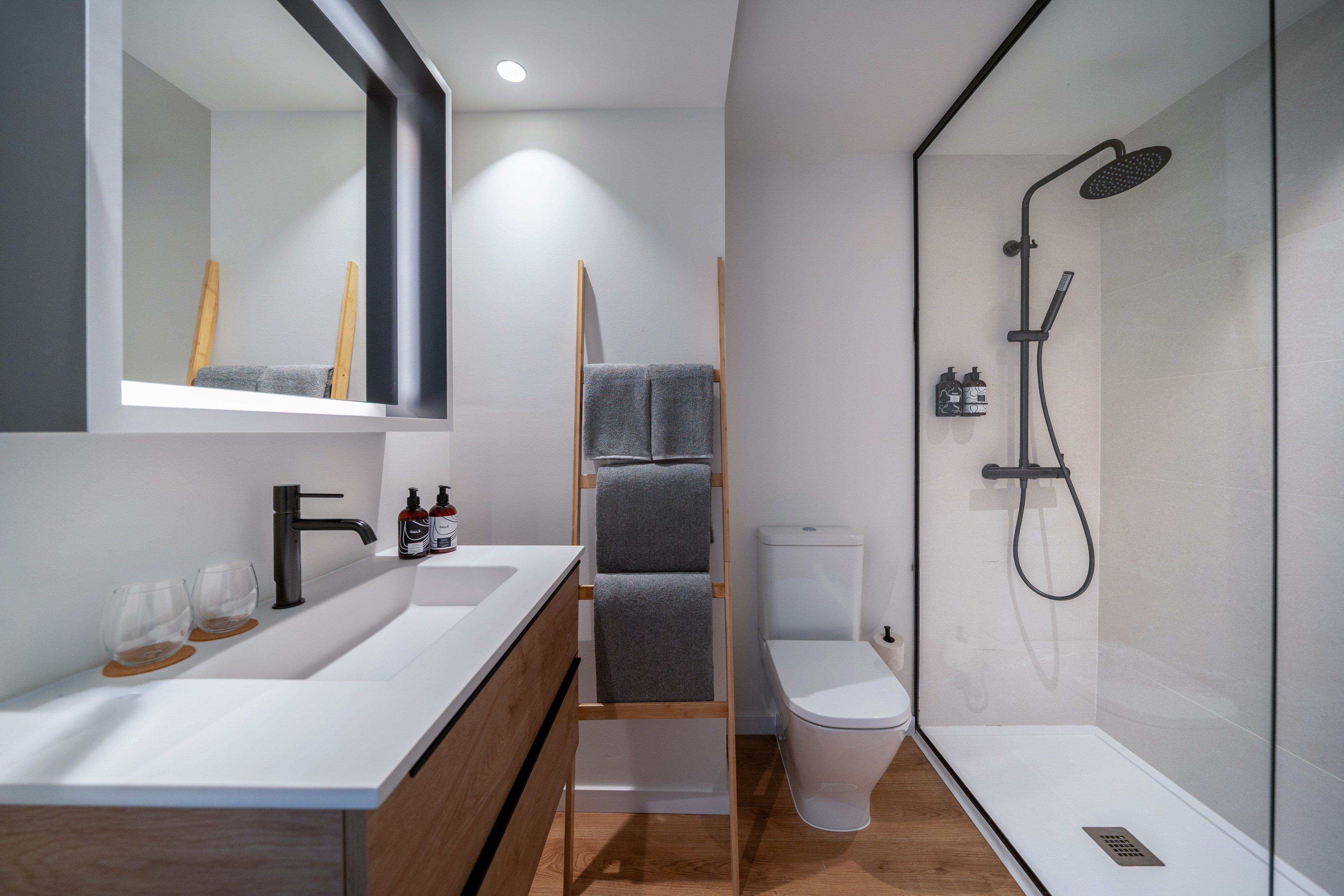 Baño moderno minimalista: lavabo madera, ducha mampara, toallero escalera.