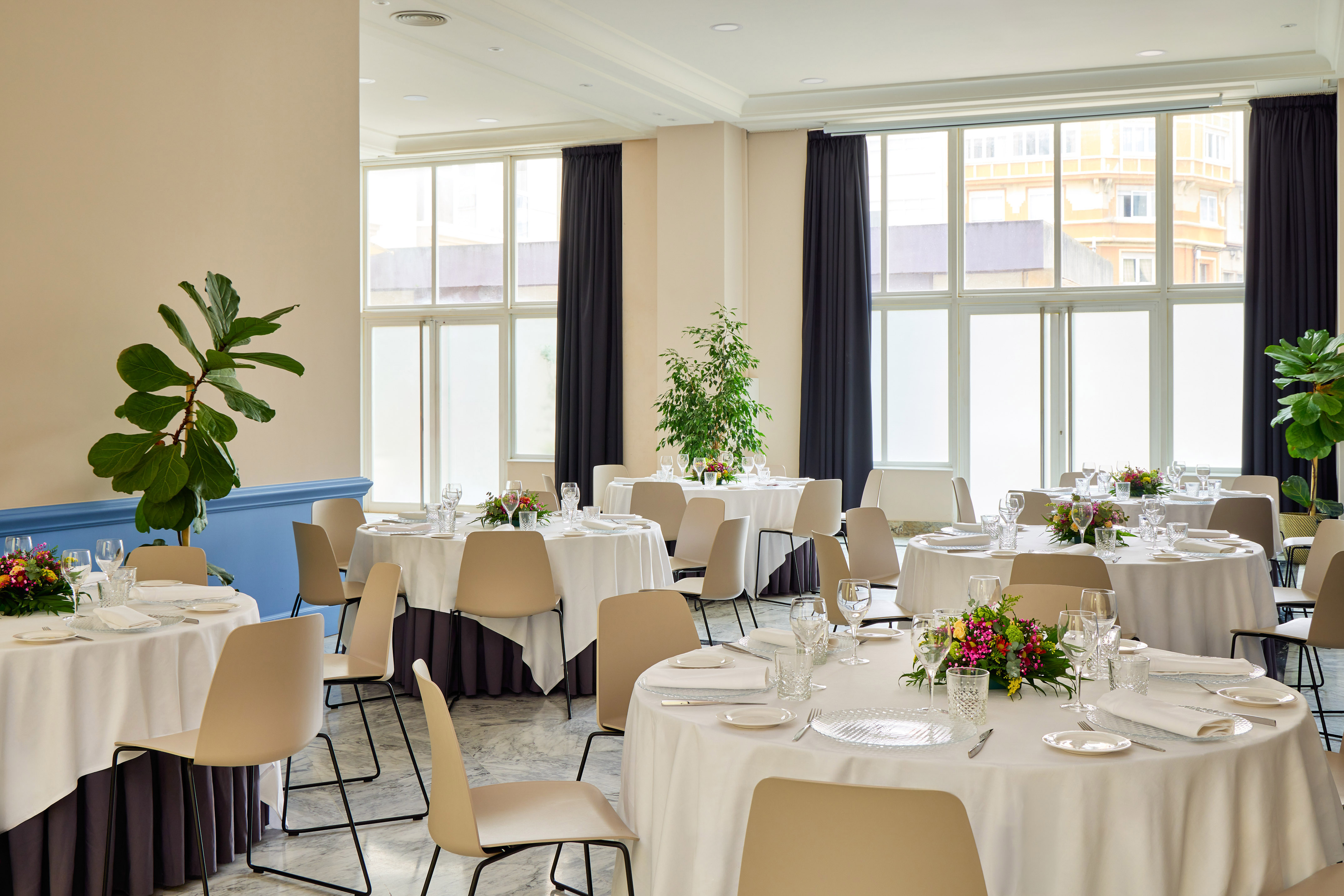 Bright event hall with set round tables, modern chairs, and large windows.