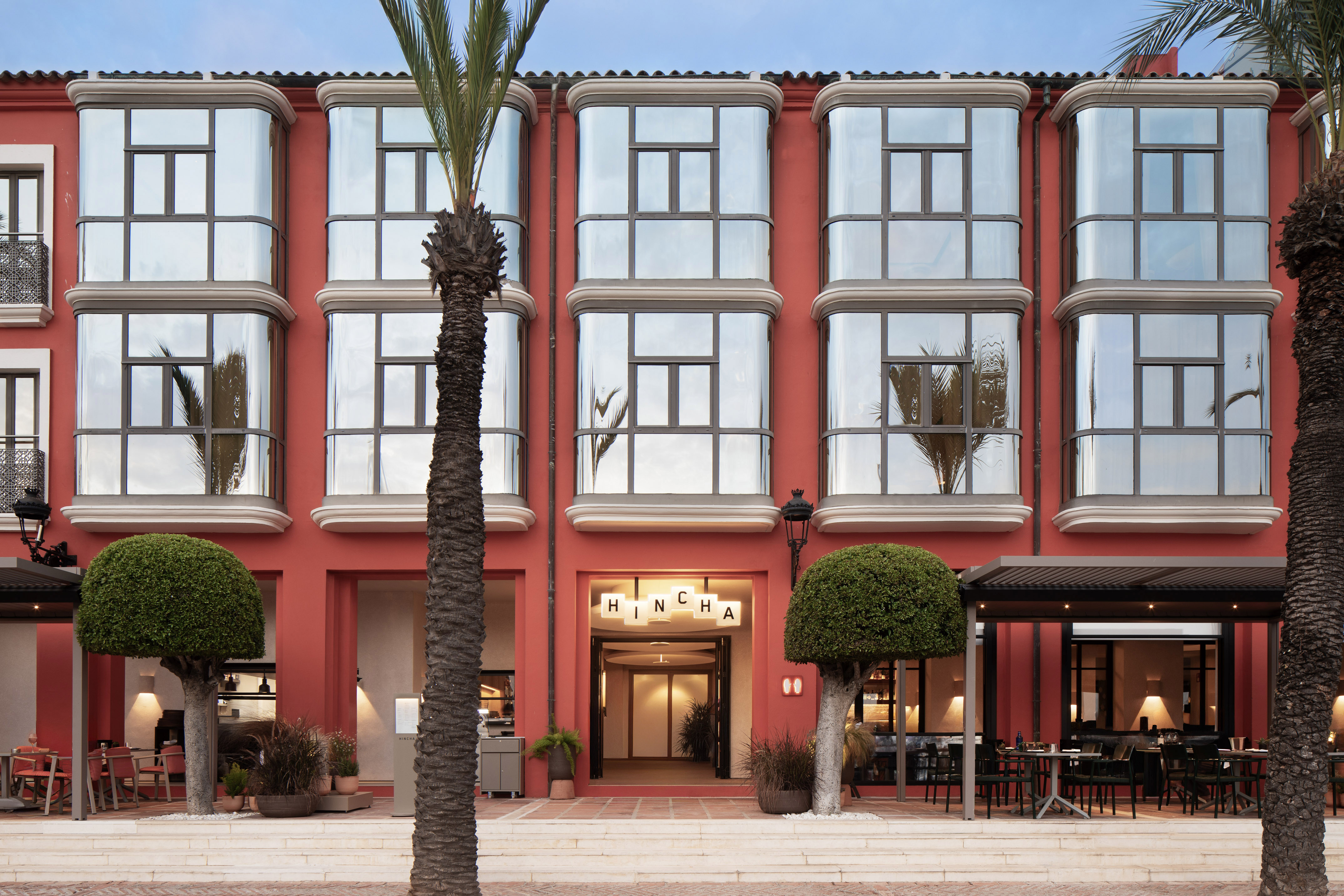 Red HINCHA restaurant exterior, modern bay windows, palm tree, outdoor dining.