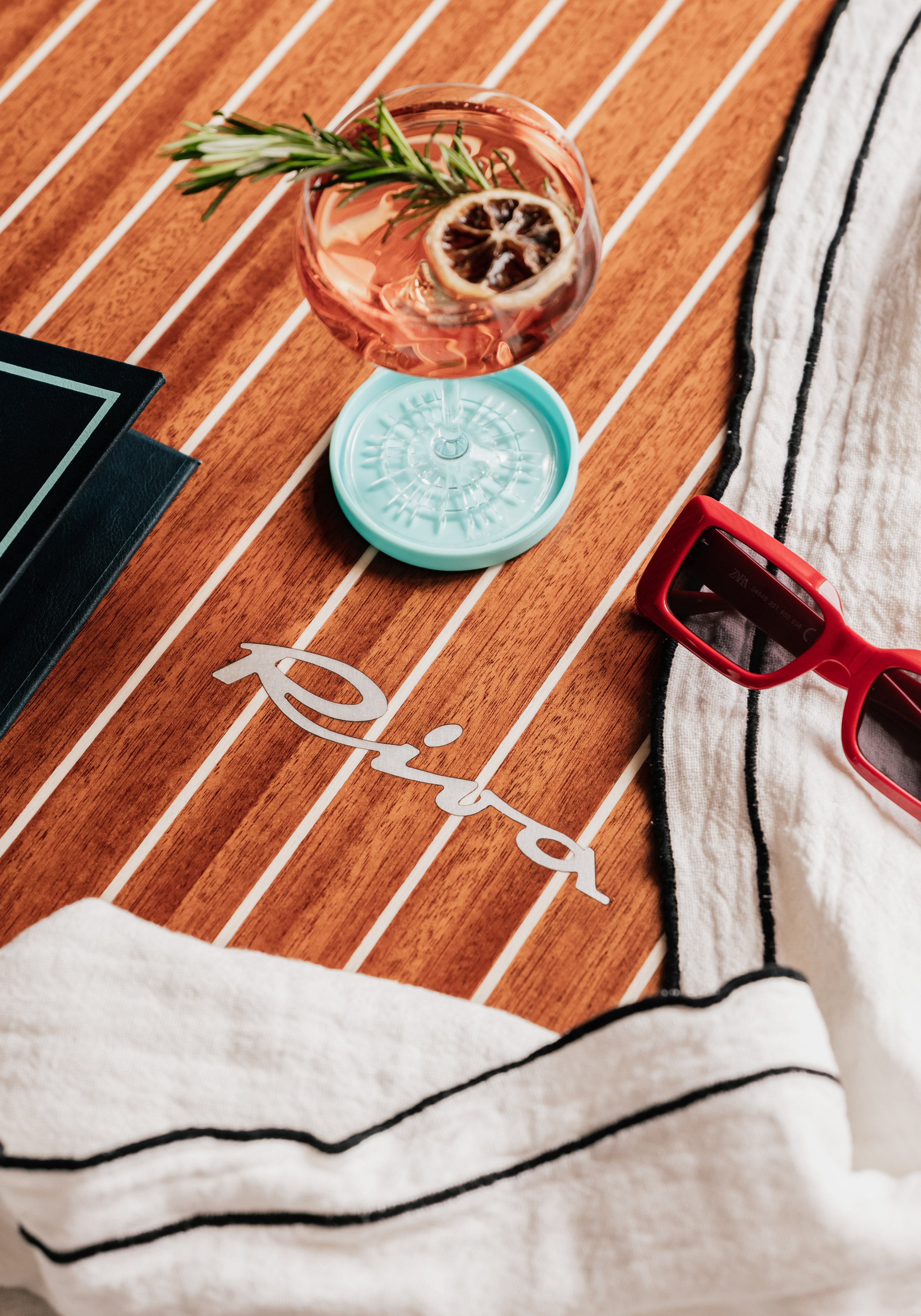 Riva boat deck with cocktail, red sunglasses, and striped towel.