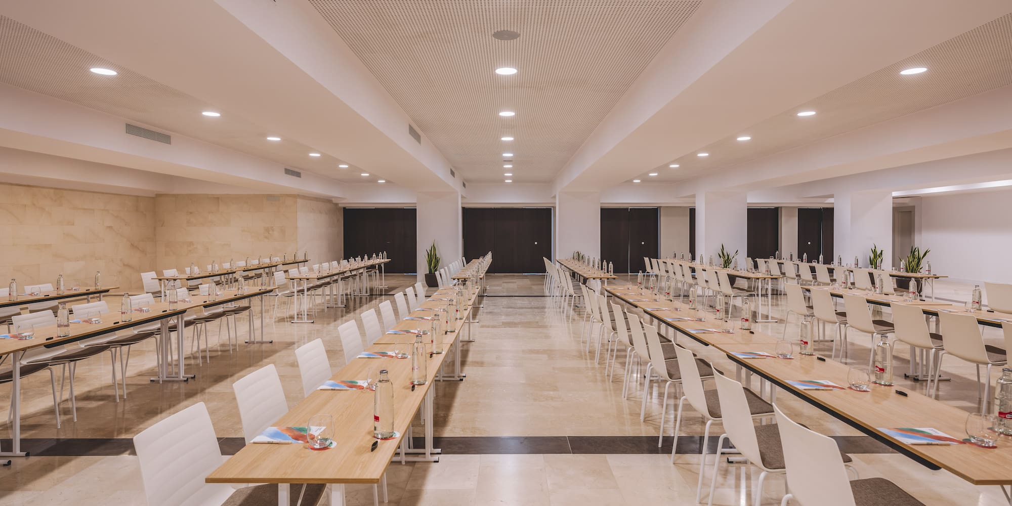 Modern conference room with long tables, chairs, and water for an event.
