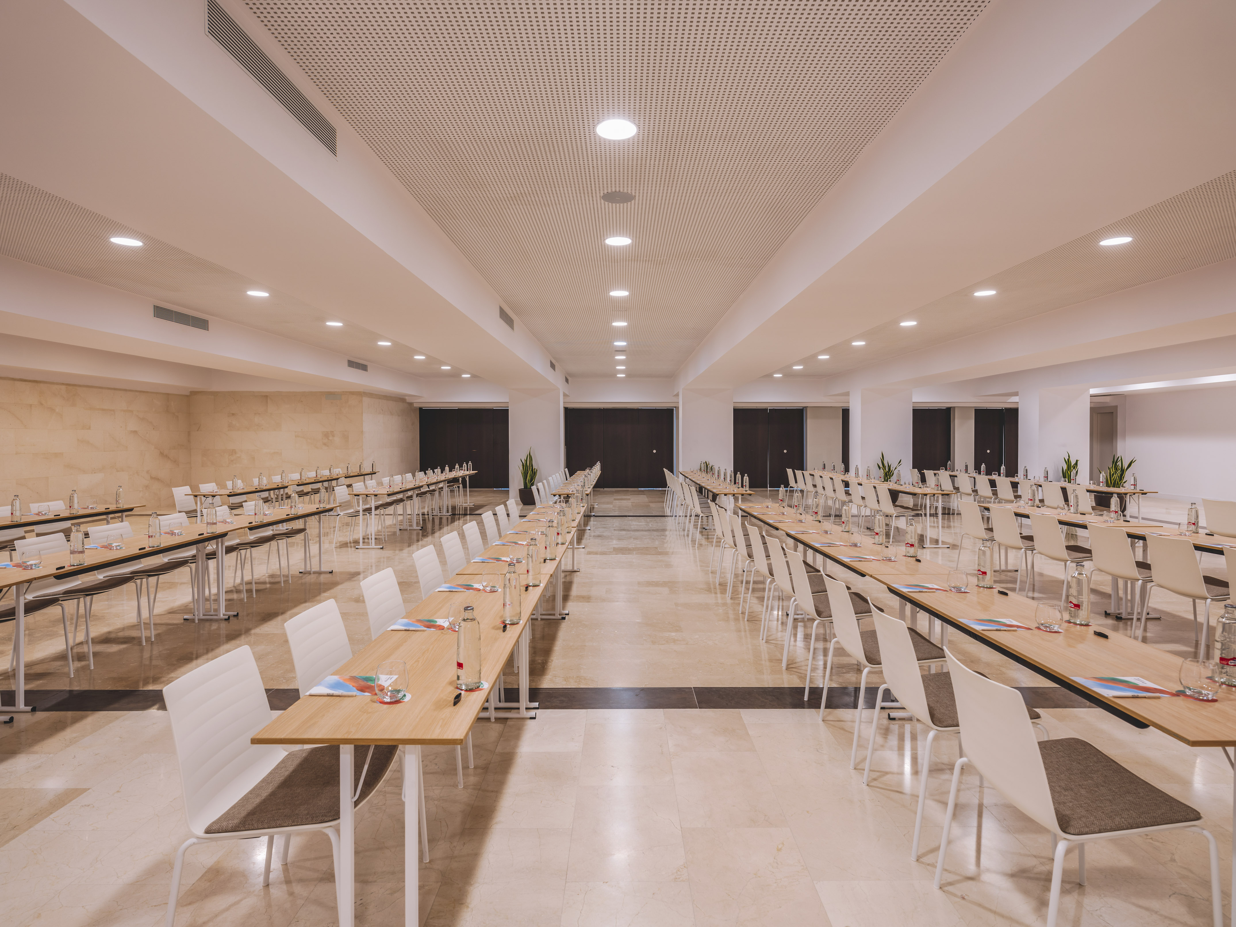 Modern conference room with long tables, chairs, and water for an event.