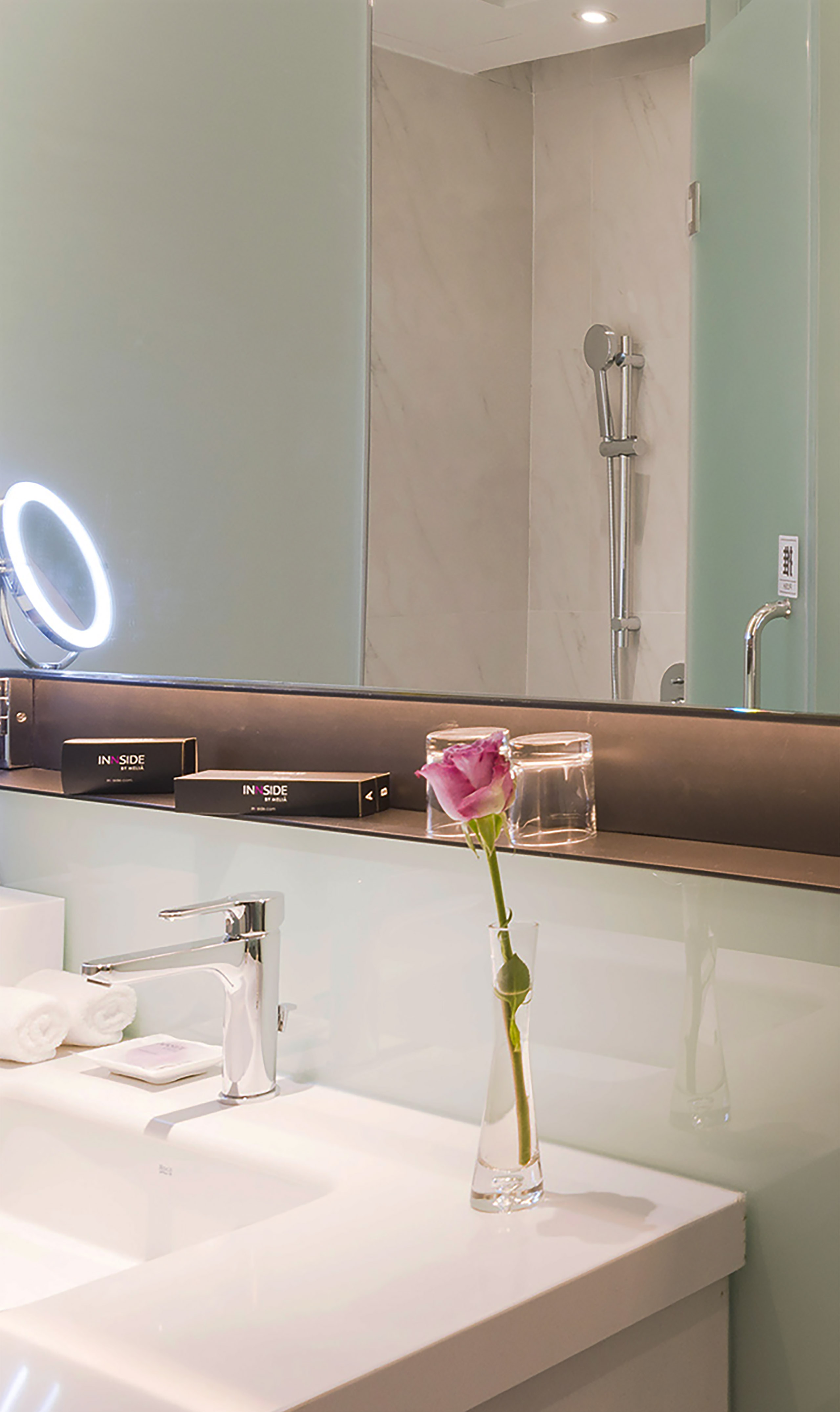 Modern hotel bathroom vanity with sink, lit mirror, rose, INNSIDE amenities.