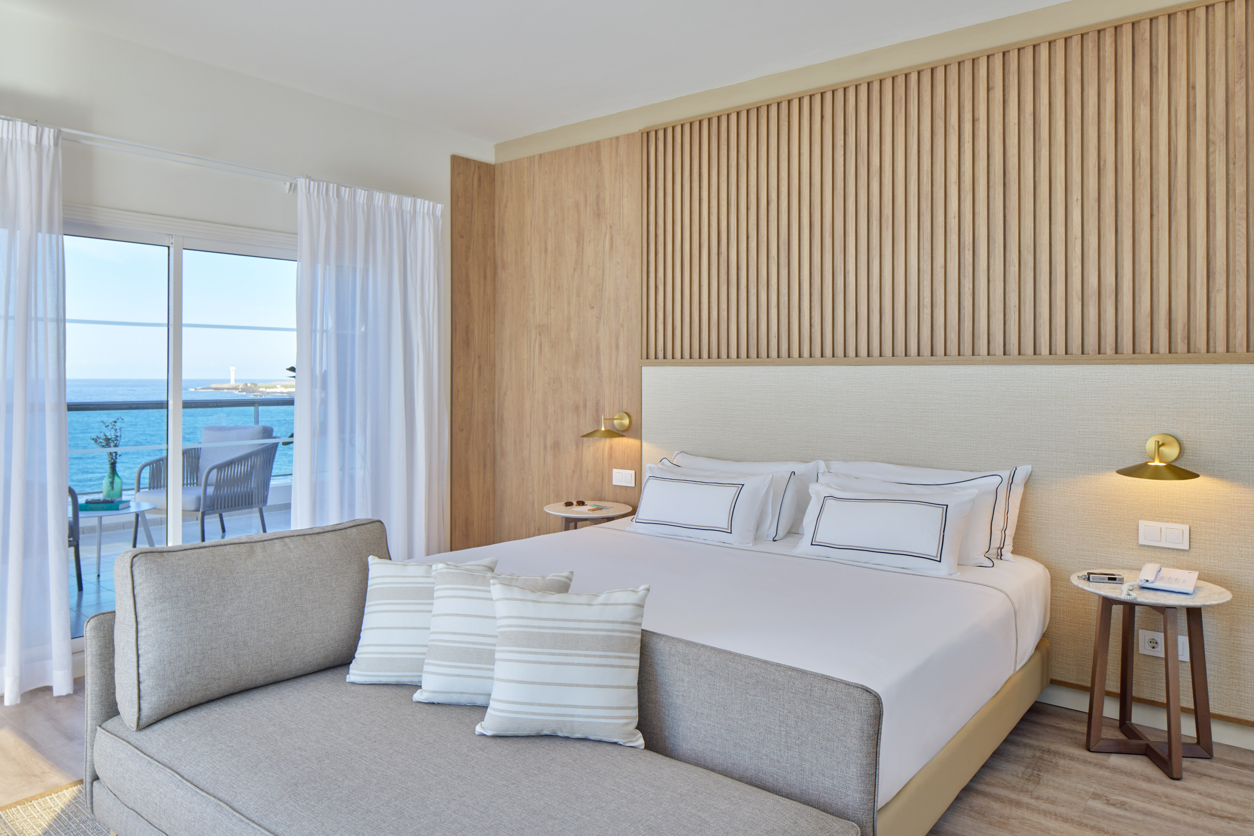 Modern hotel room with ocean view balcony, large bed, and wood accent wall.