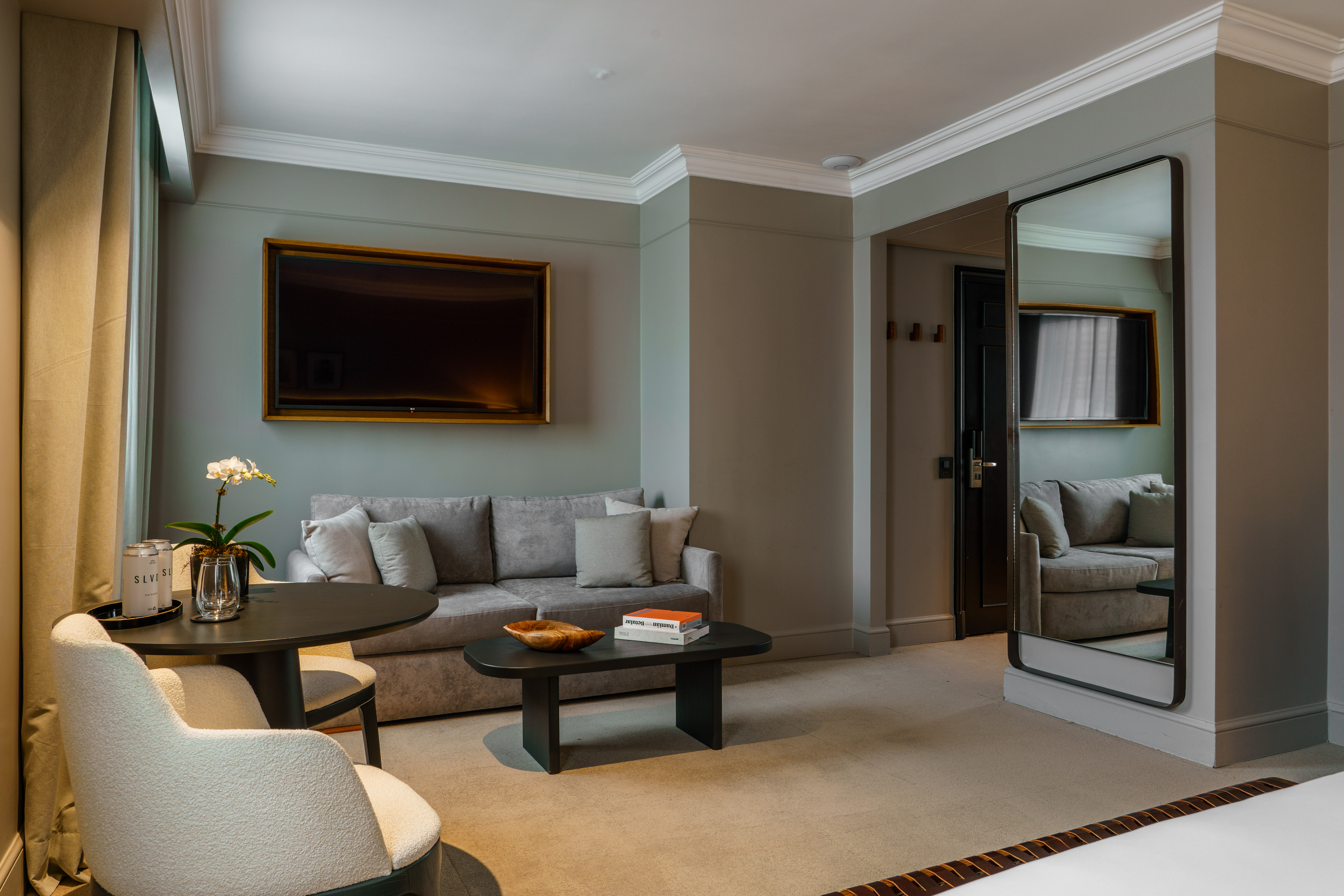 Hotel suite living area with gray sofa, wall-mounted TV, coffee table, and dining set.