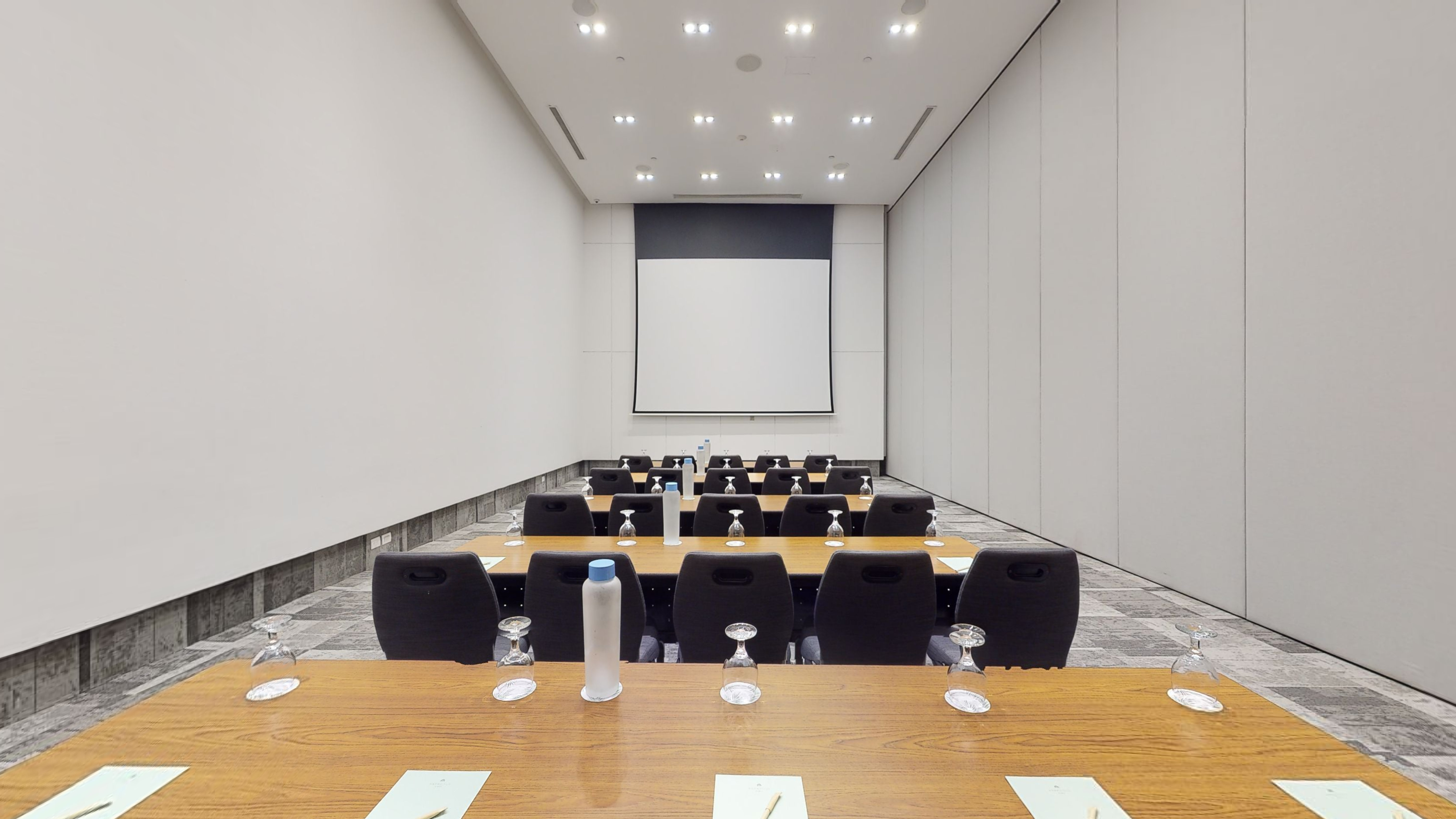 Modern meeting room with tables, chairs, and large presentation screen.
