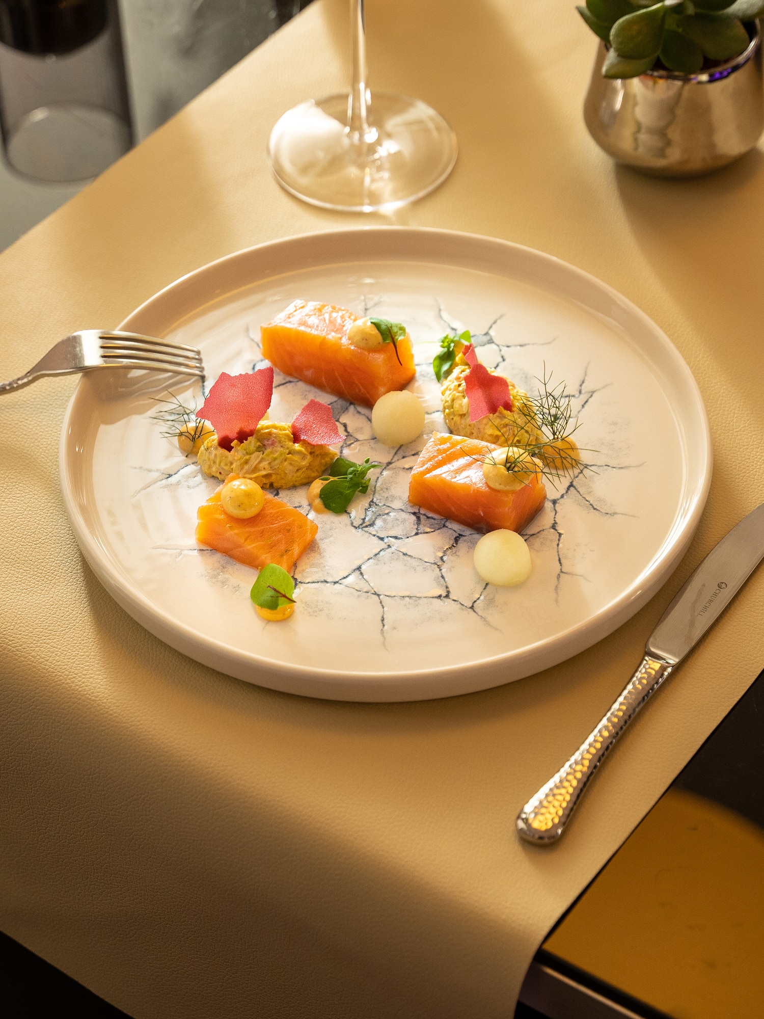 Gourmet salmon appetizer on patterned plate with colorful garnishes and wine.