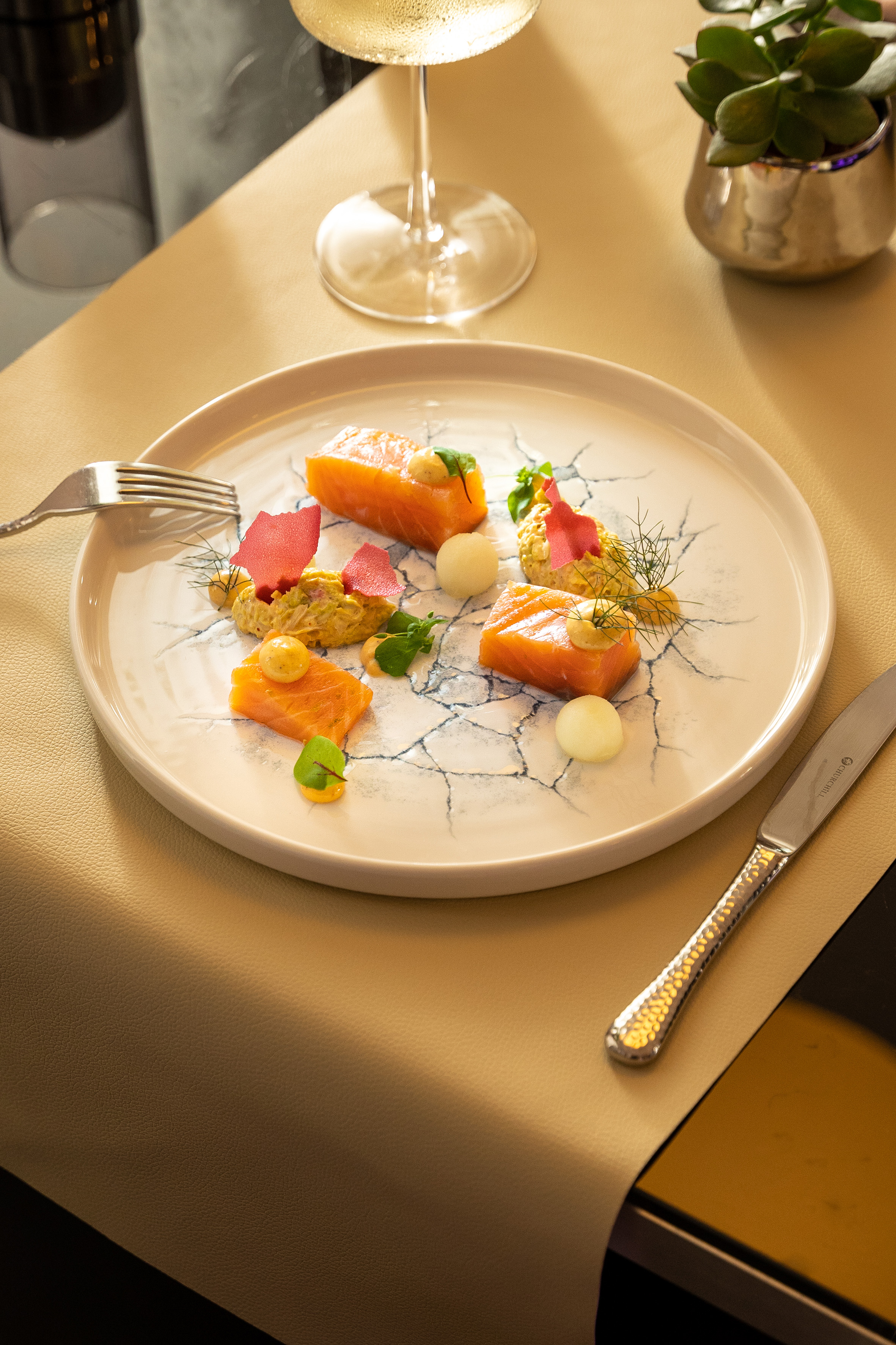 Gourmet salmon appetizer on patterned plate with colorful garnishes and wine.