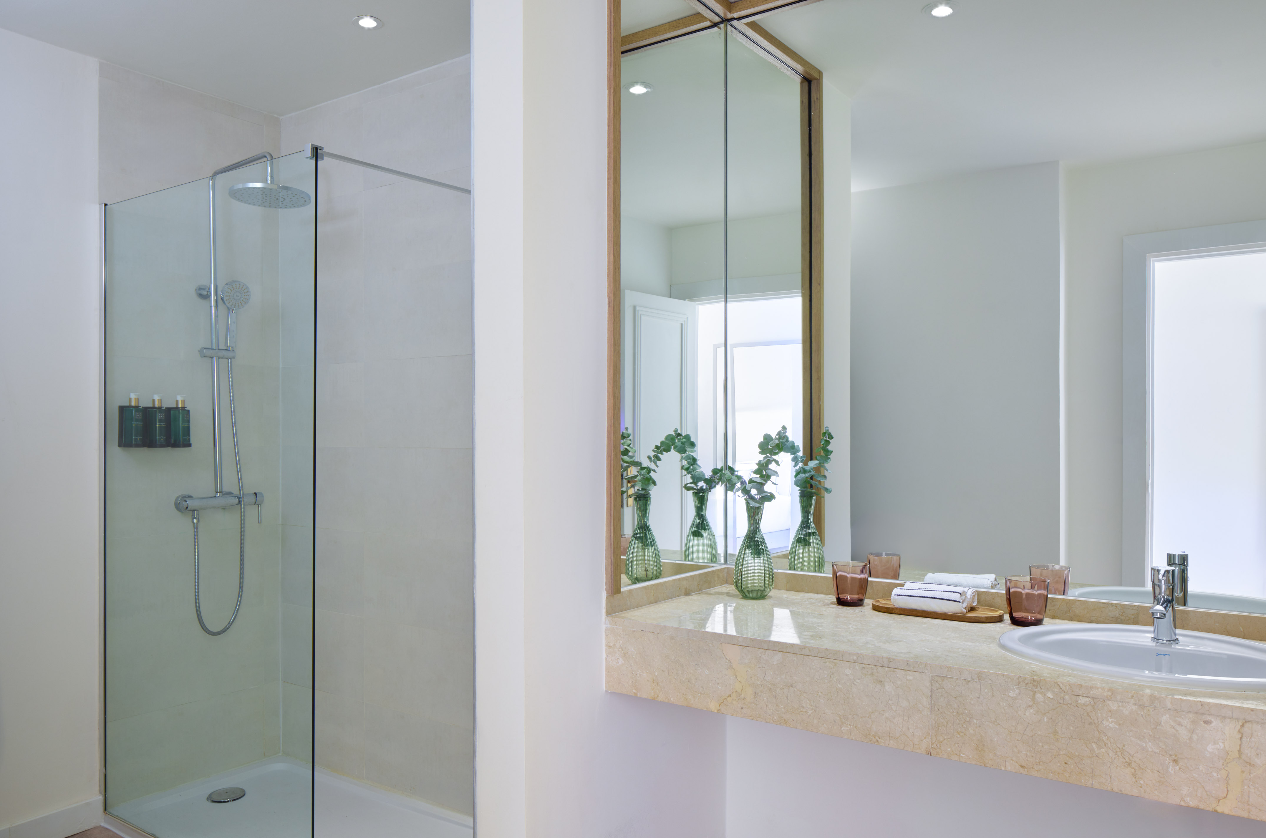 Modern hotel bathroom with glass shower, marble vanity, sink, and large mirror.