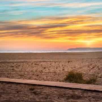 a beach with a wooden walkway and a sunset