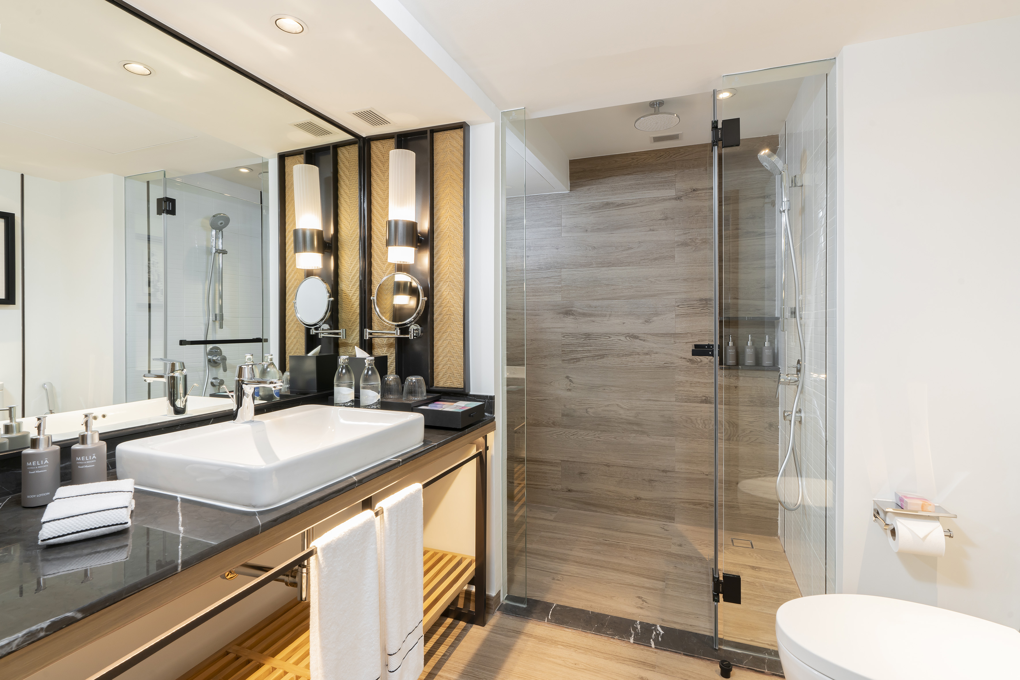 Modern hotel bathroom with vanity, glass shower, and wood accents.