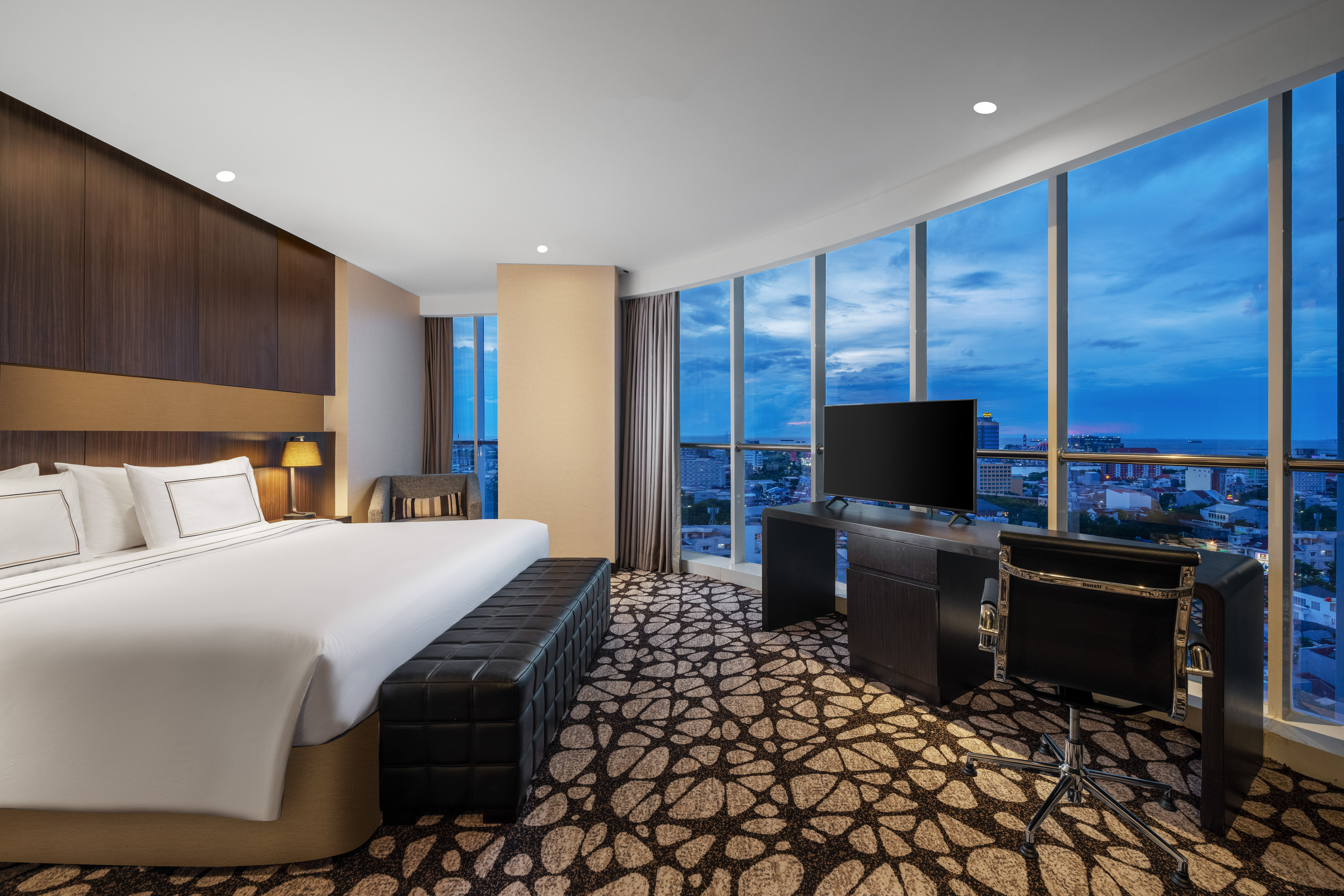 Modern hotel room with king bed, desk, TV, and panoramic city/sea view.