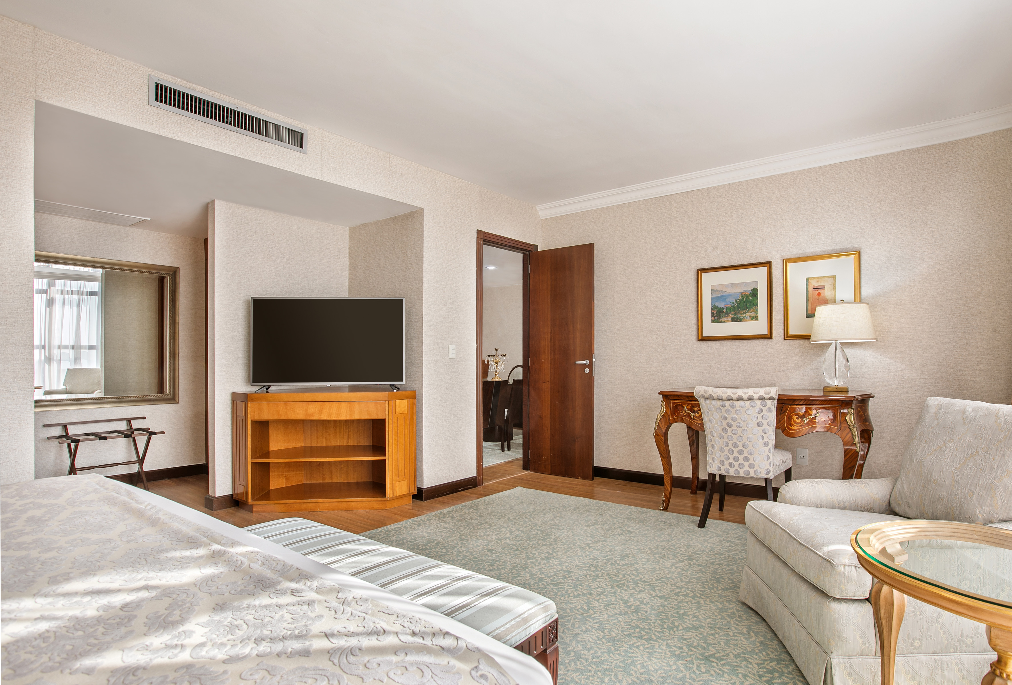 Elegant hotel bedroom with TV, classic desk, and cozy armchair.