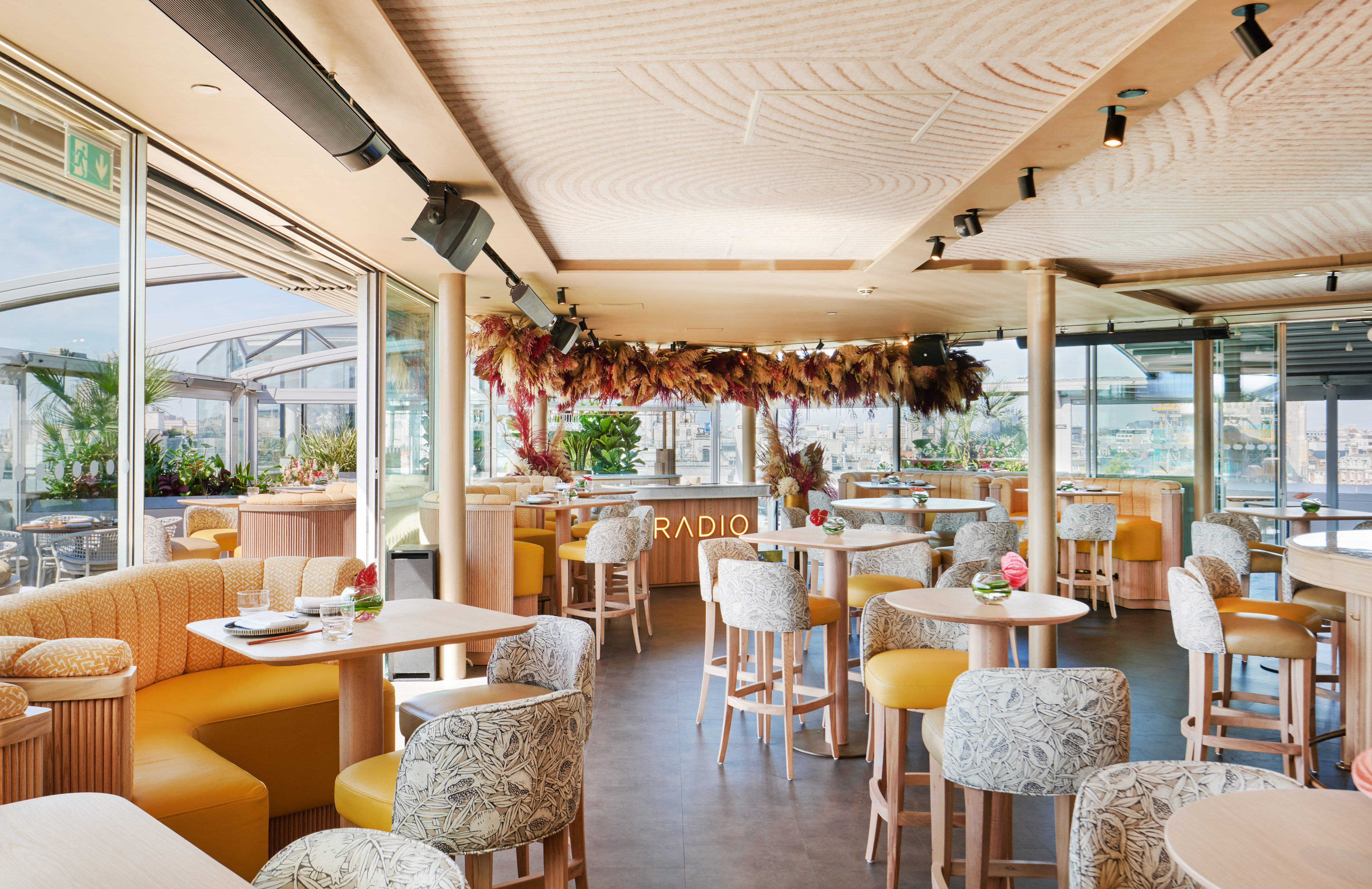 Rooftop bar & restaurant with yellow seating, dried floral decor, and city views.