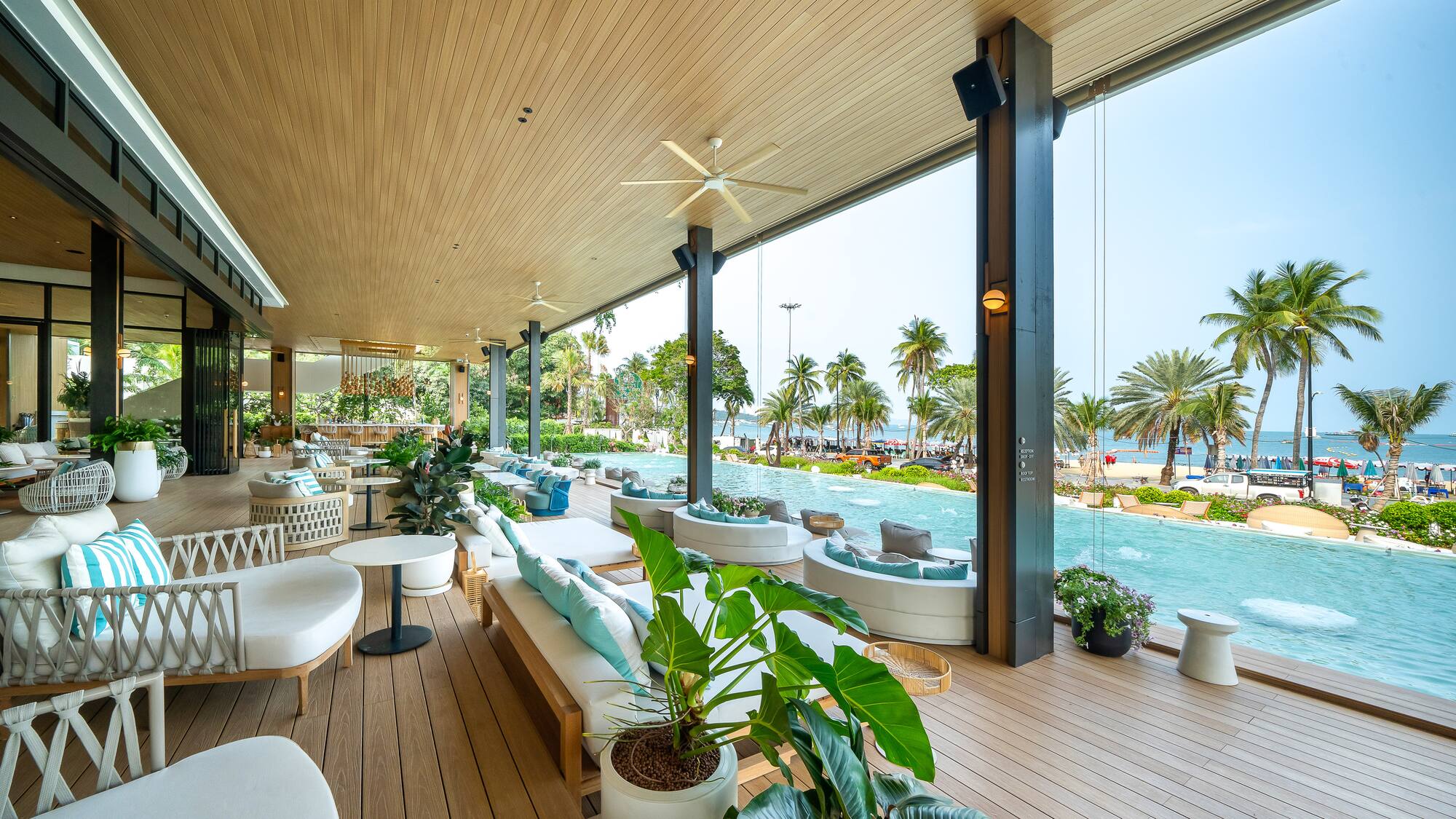 Modern hotel lounge with infinity pool, ocean view, and palm-lined beach.