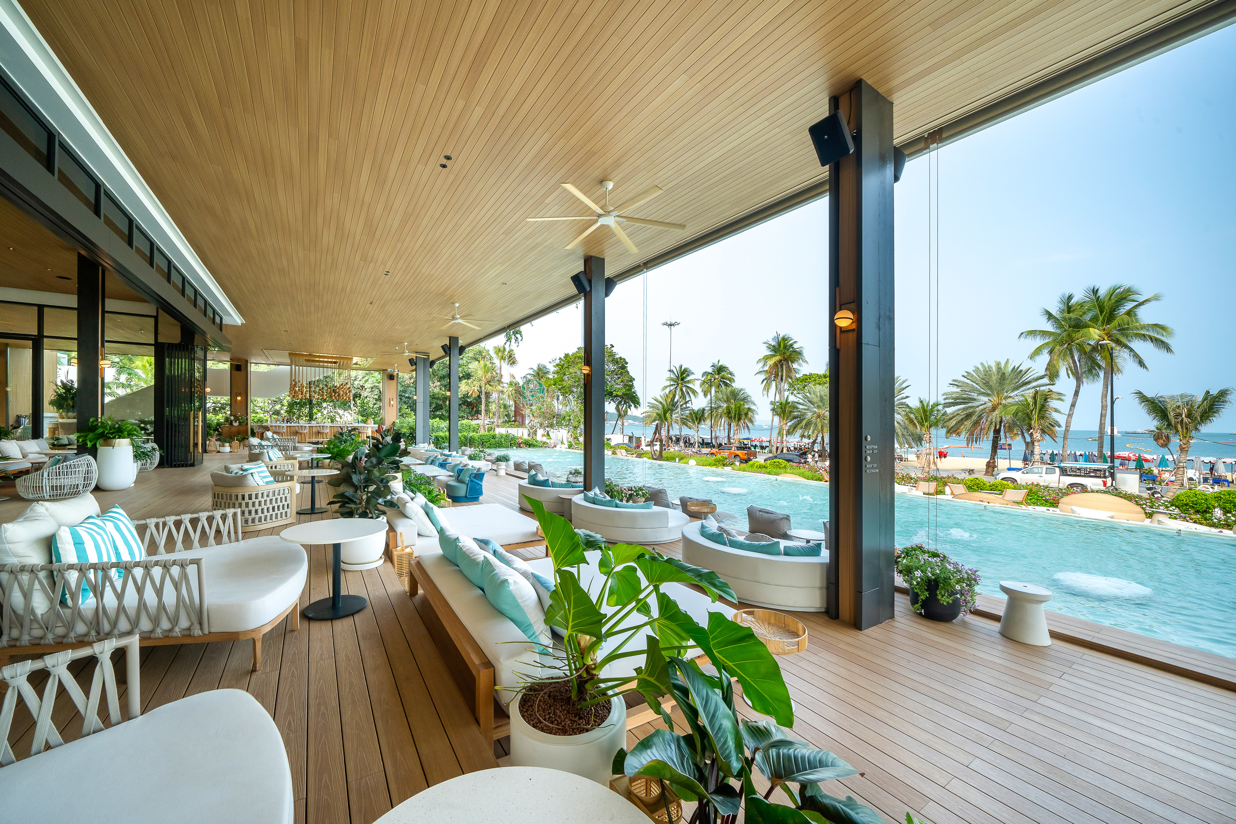Modern hotel lounge with infinity pool, ocean view, and palm-lined beach.