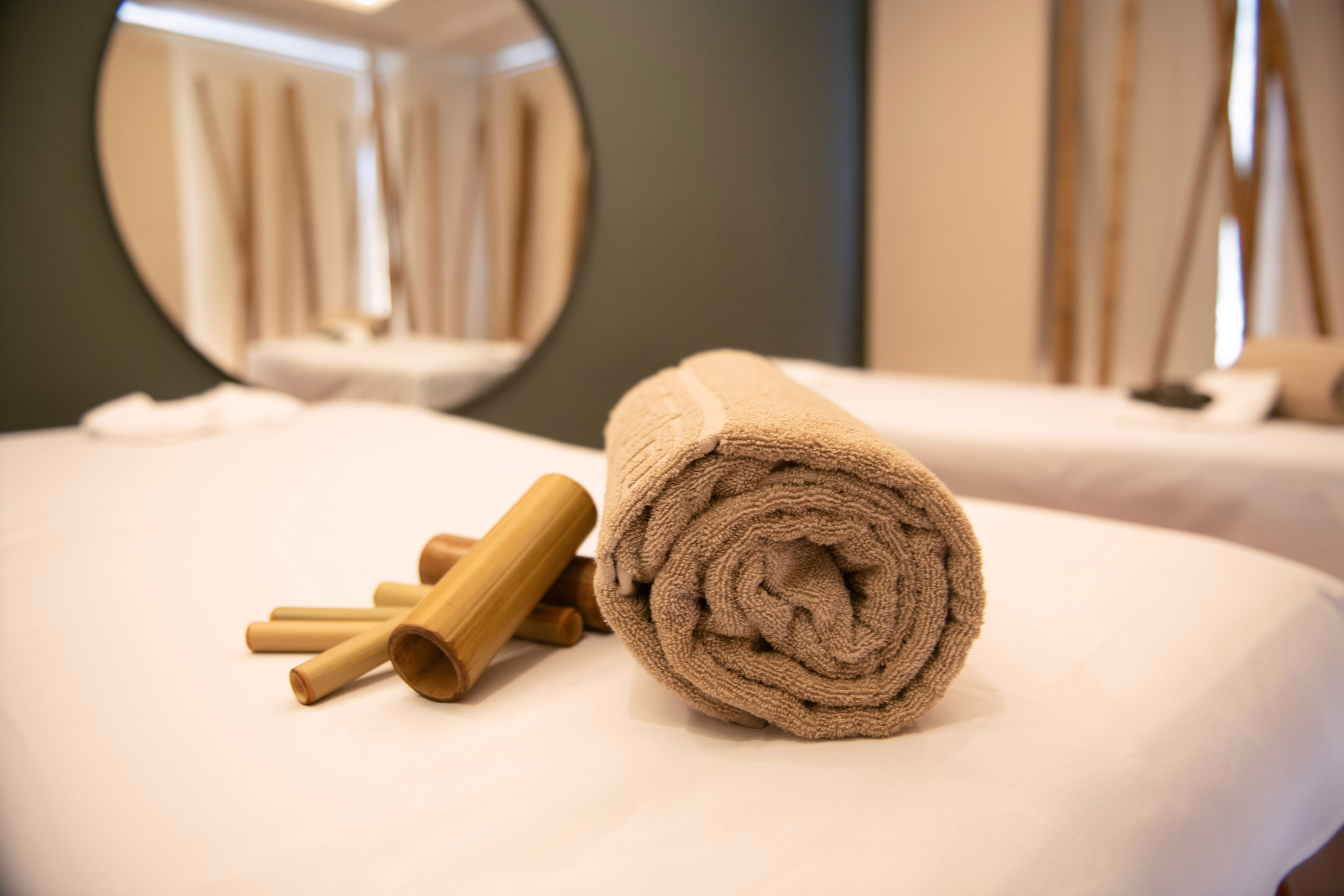 Beige rolled towel and bamboo sticks on a white spa massage bed.