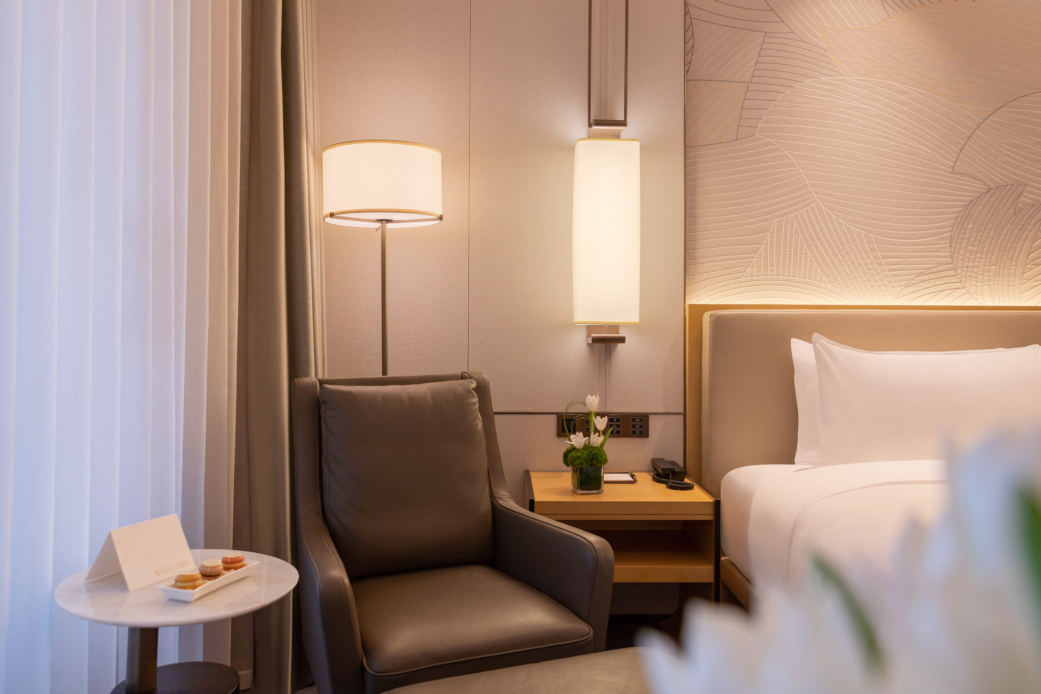 Elegant hotel room with comfy bed, modern armchair, warm lighting, welcome treat.