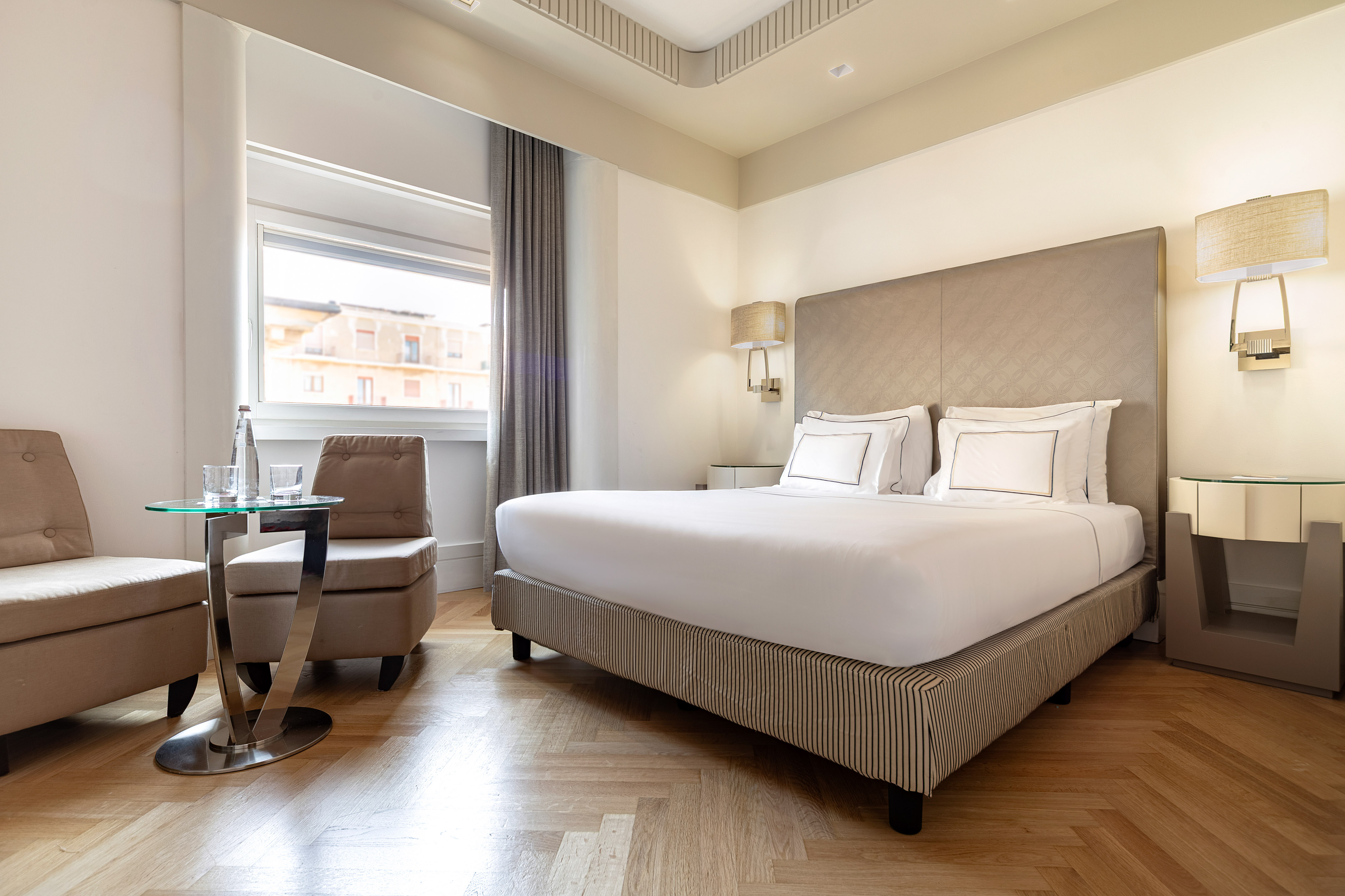 Modern hotel bedroom with king bed, comfortable seating, and window.