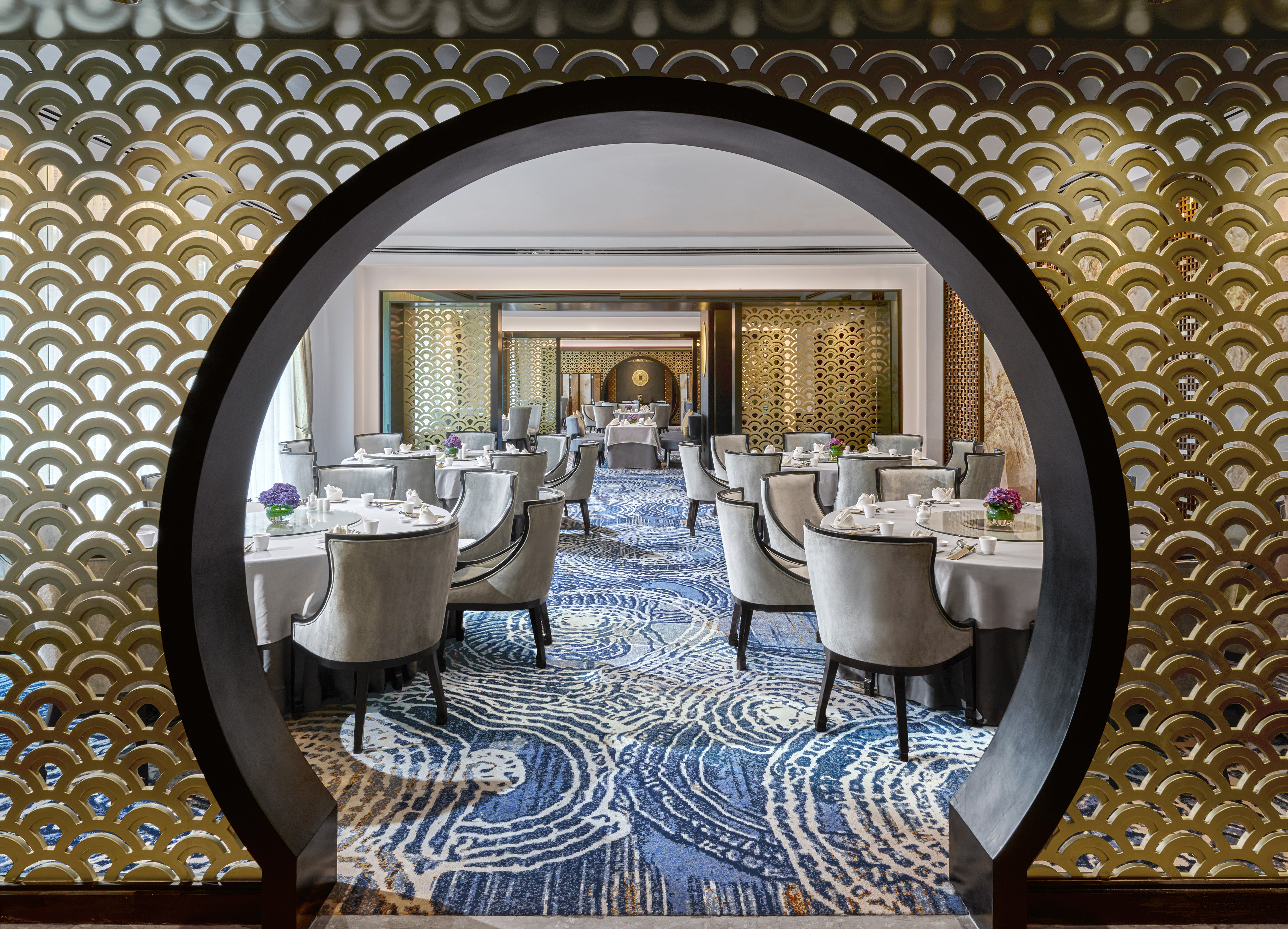 Elegant dining room, circular archway, golden decorative screens, and blue patterned carpet.