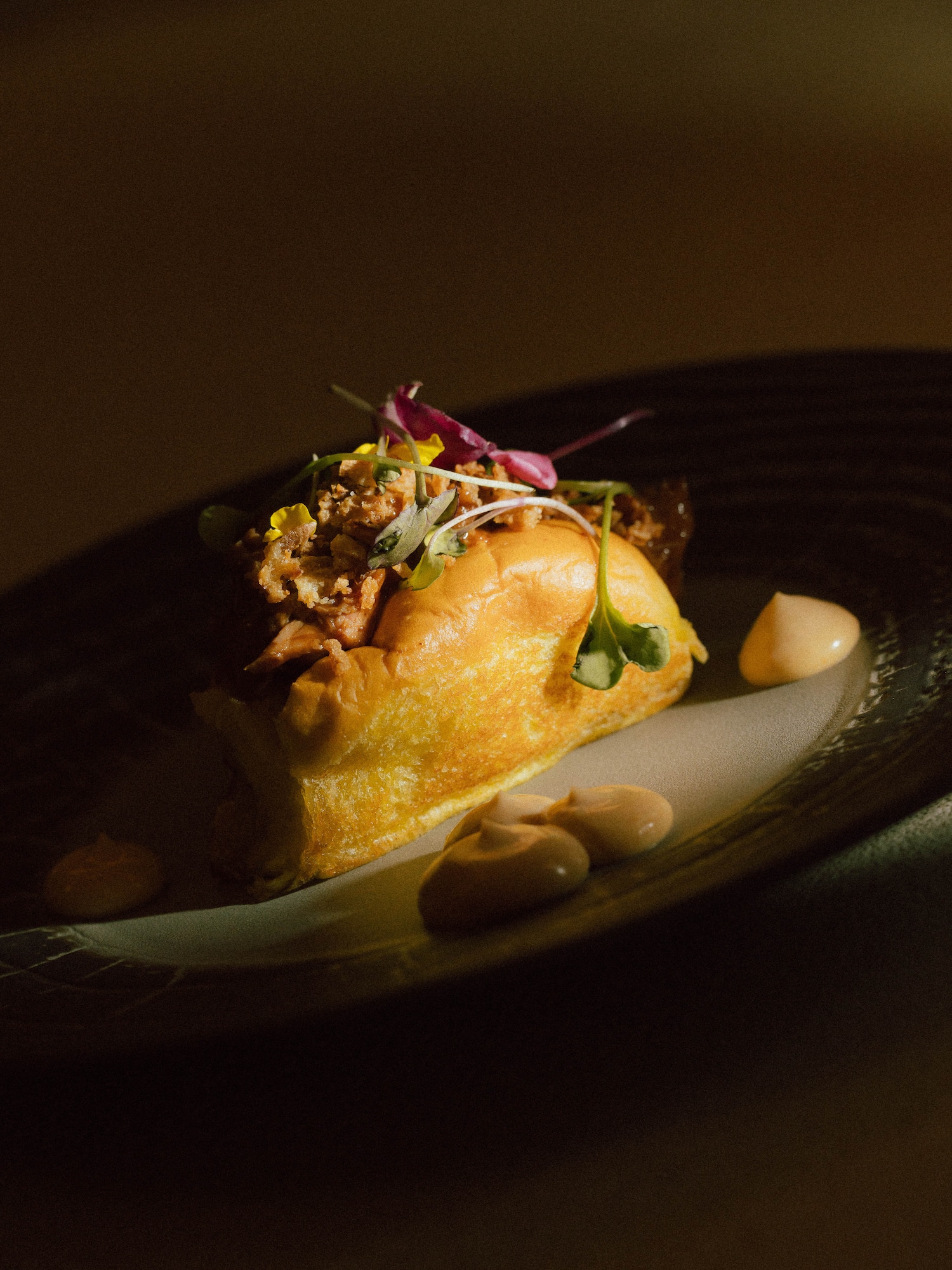 Gourmet pulled meat slider with crispy topping, microgreens, and creamy sauce.
