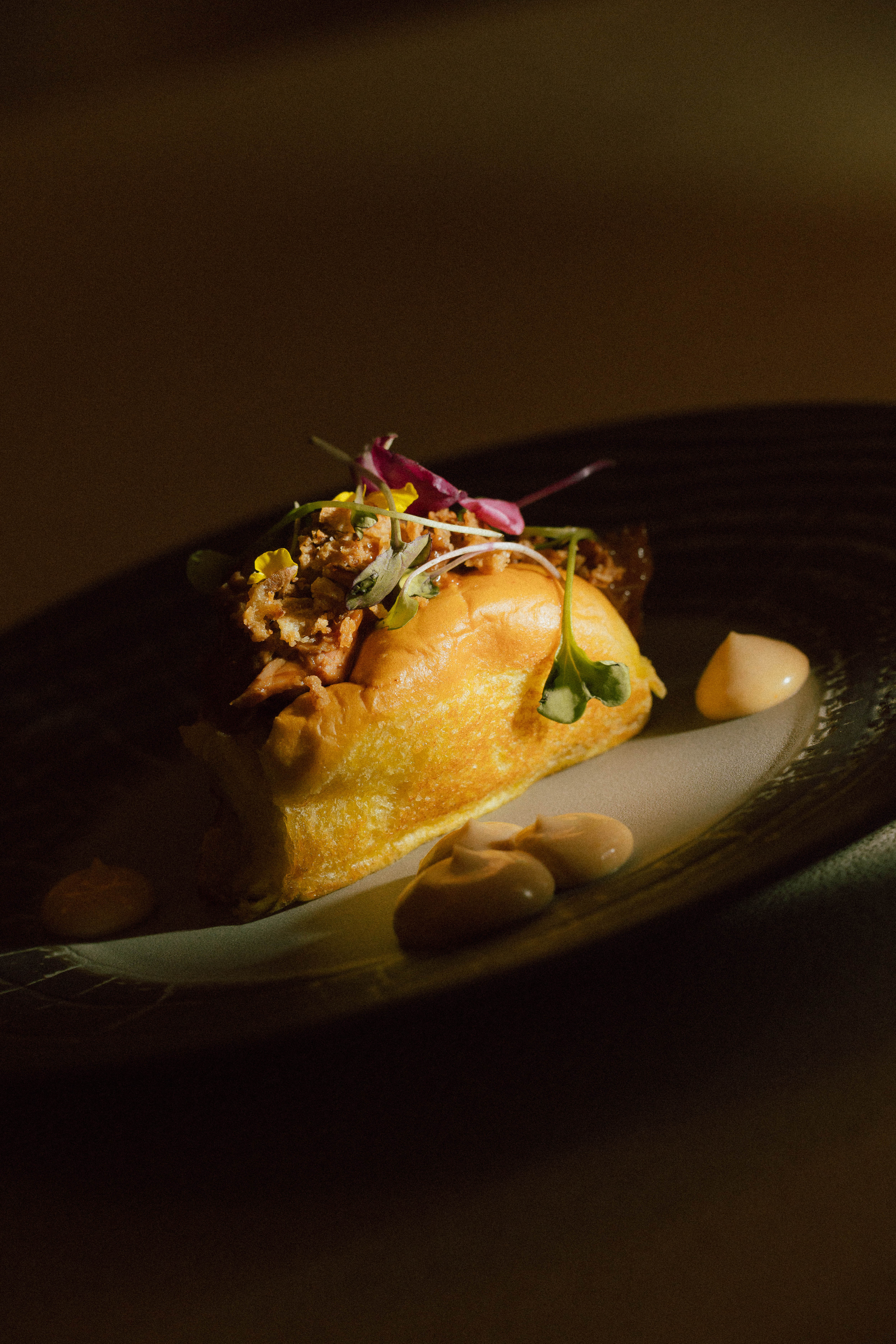 Gourmet pulled meat slider with crispy topping, microgreens, and creamy sauce.