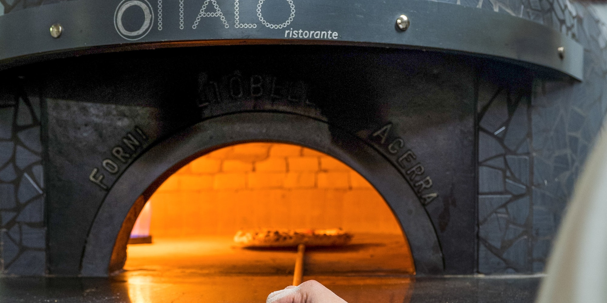 a hand holding a blue pen in a pizza oven