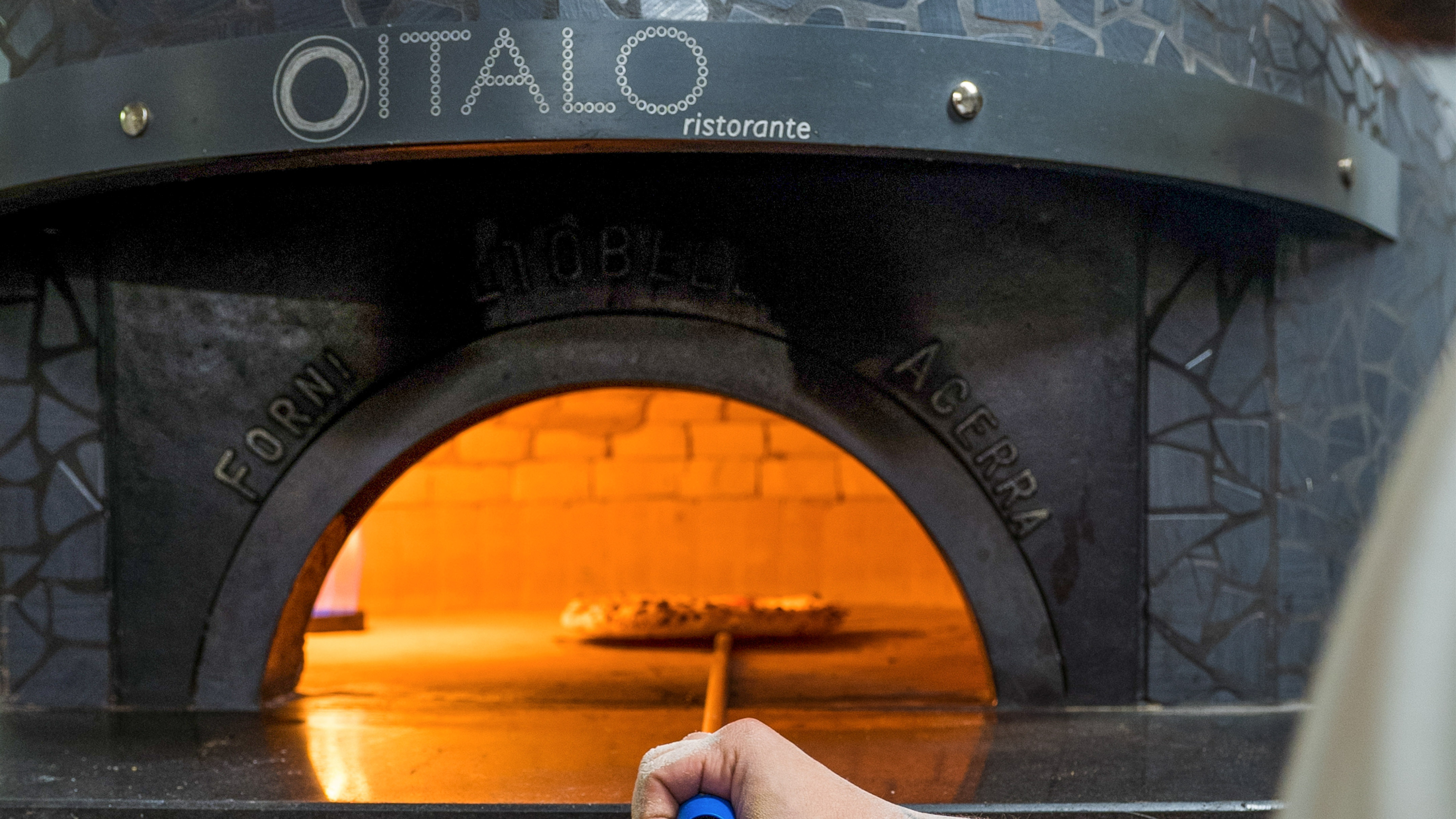 Hand placing pizza into hot ITALO ristorante wood-fired oven.