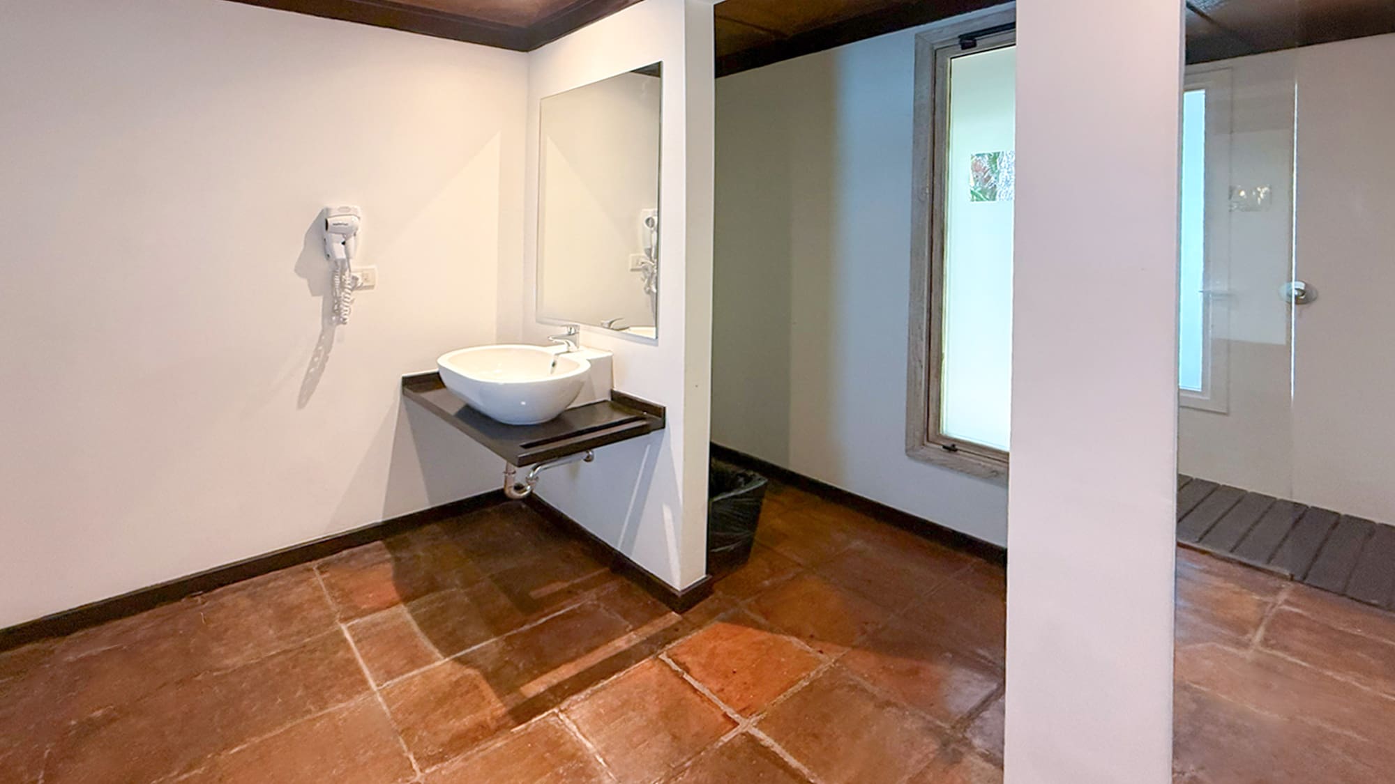 Clean bathroom with white sink, large mirror, terracotta floor, and shower.