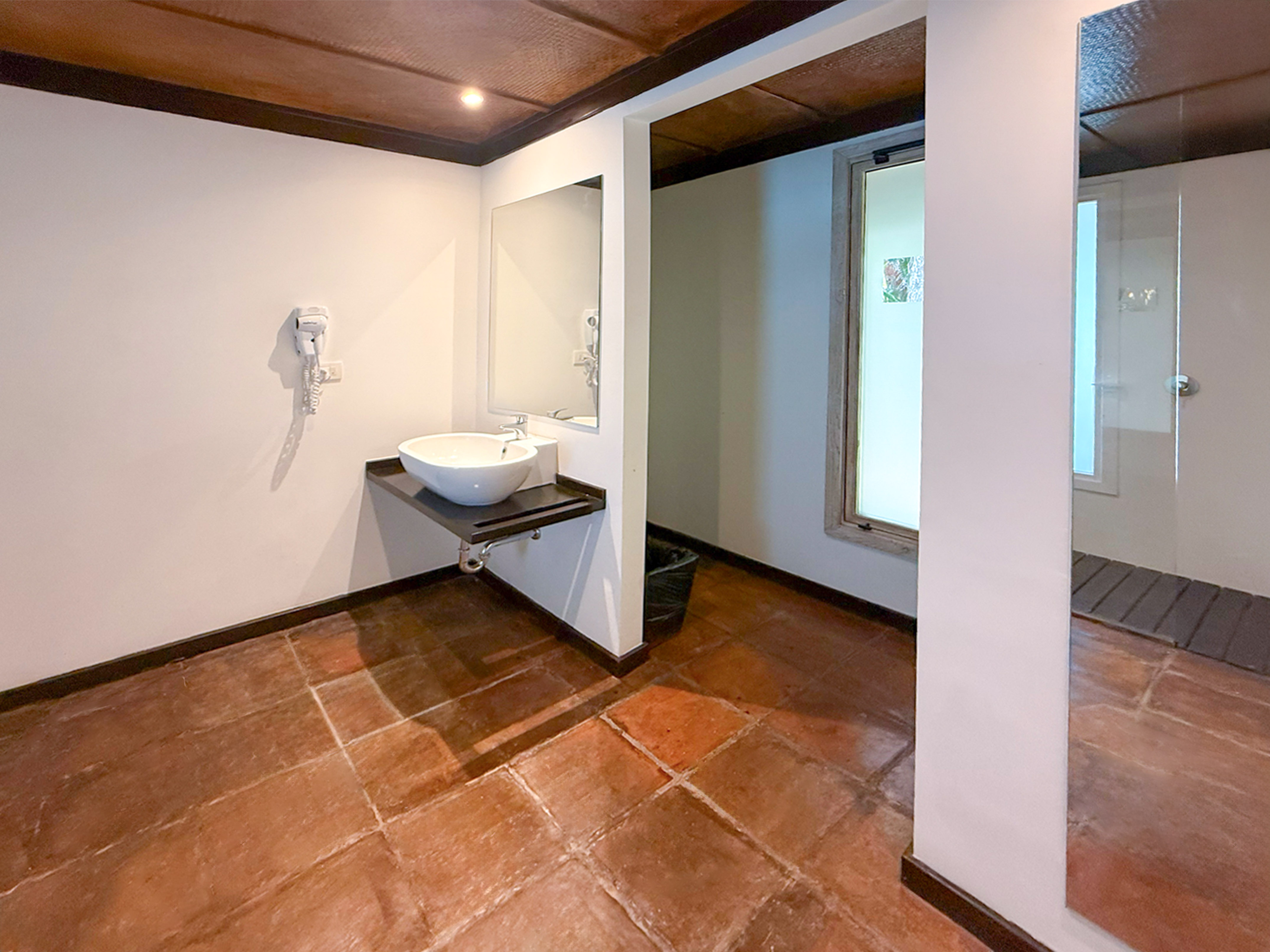 Clean bathroom with white sink, large mirror, terracotta floor, and shower.