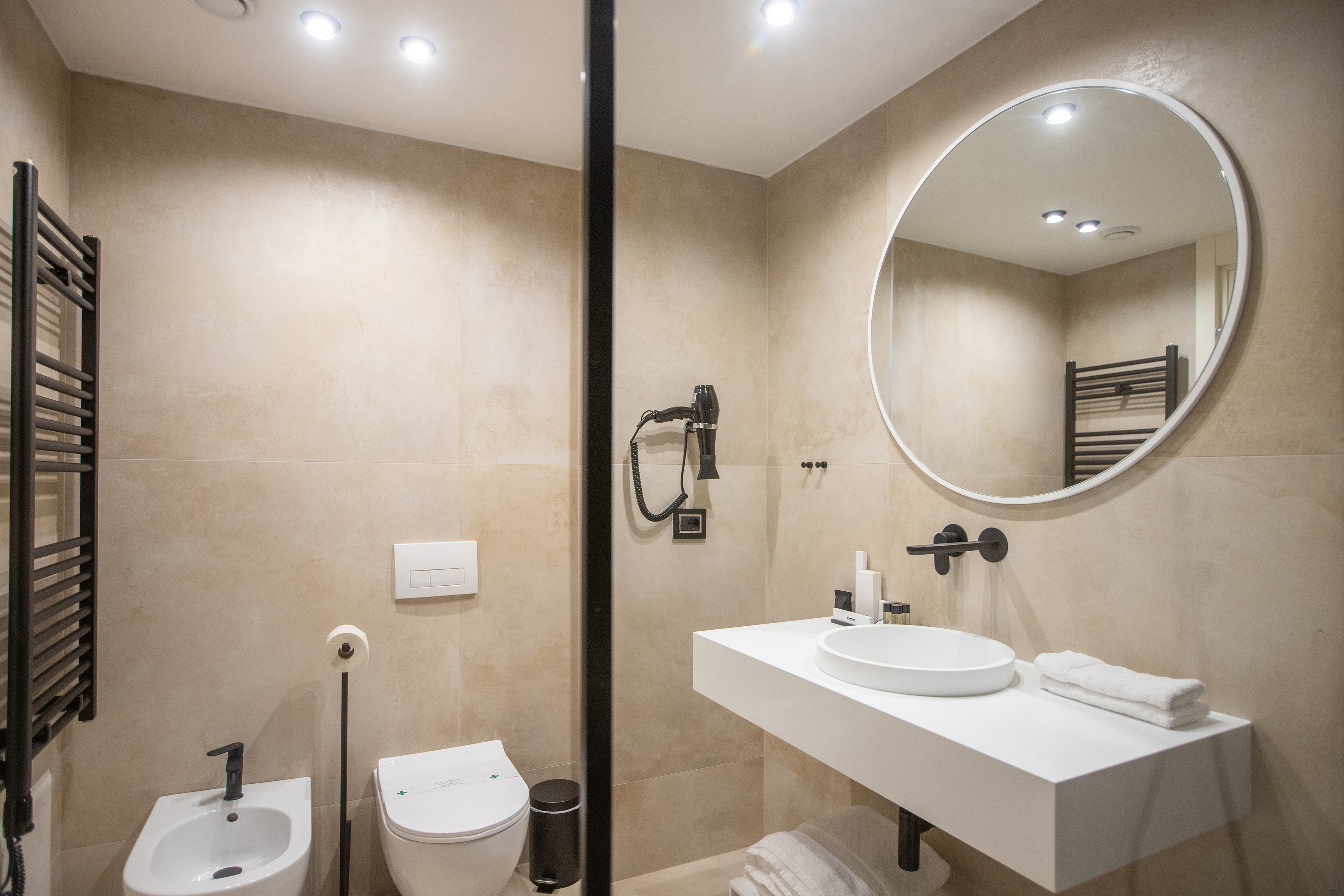 Modern beige bathroom with white sink, round mirror, black accents.